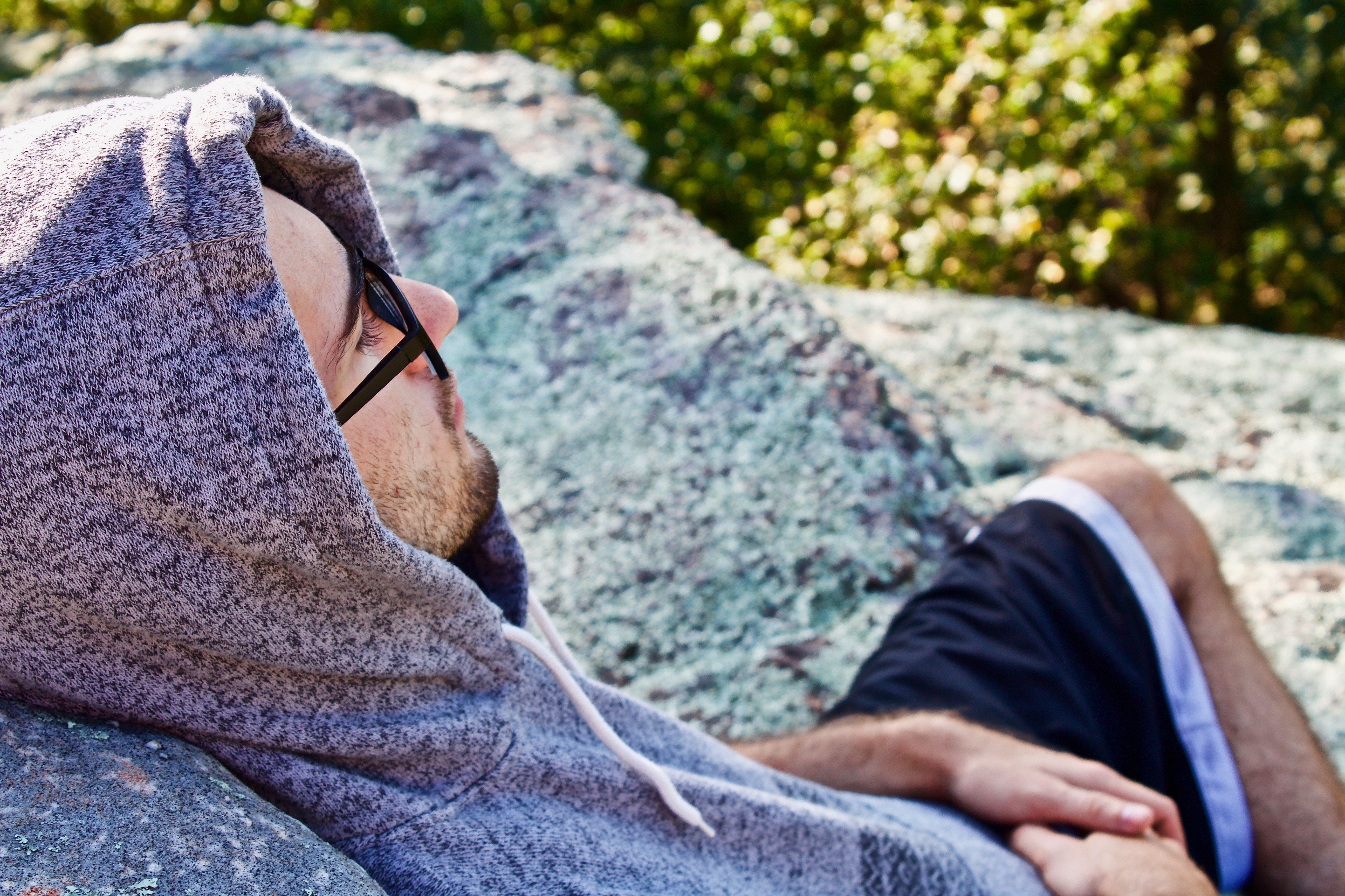 Man in hoodie relaxing on a rock HD Wallpaper