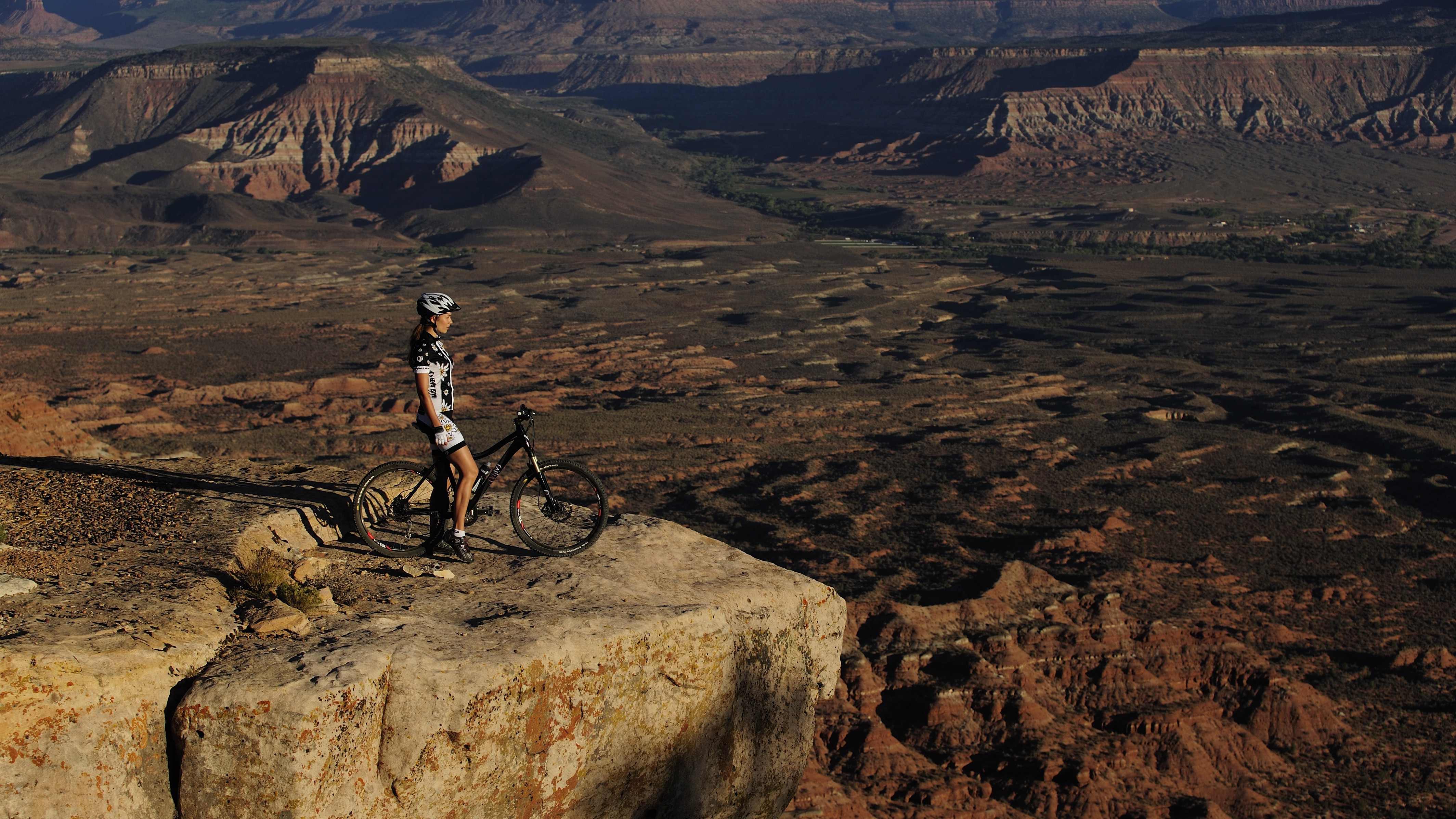Woman with mountain bike on cliff edge overlooking canyon HD Wallpaper