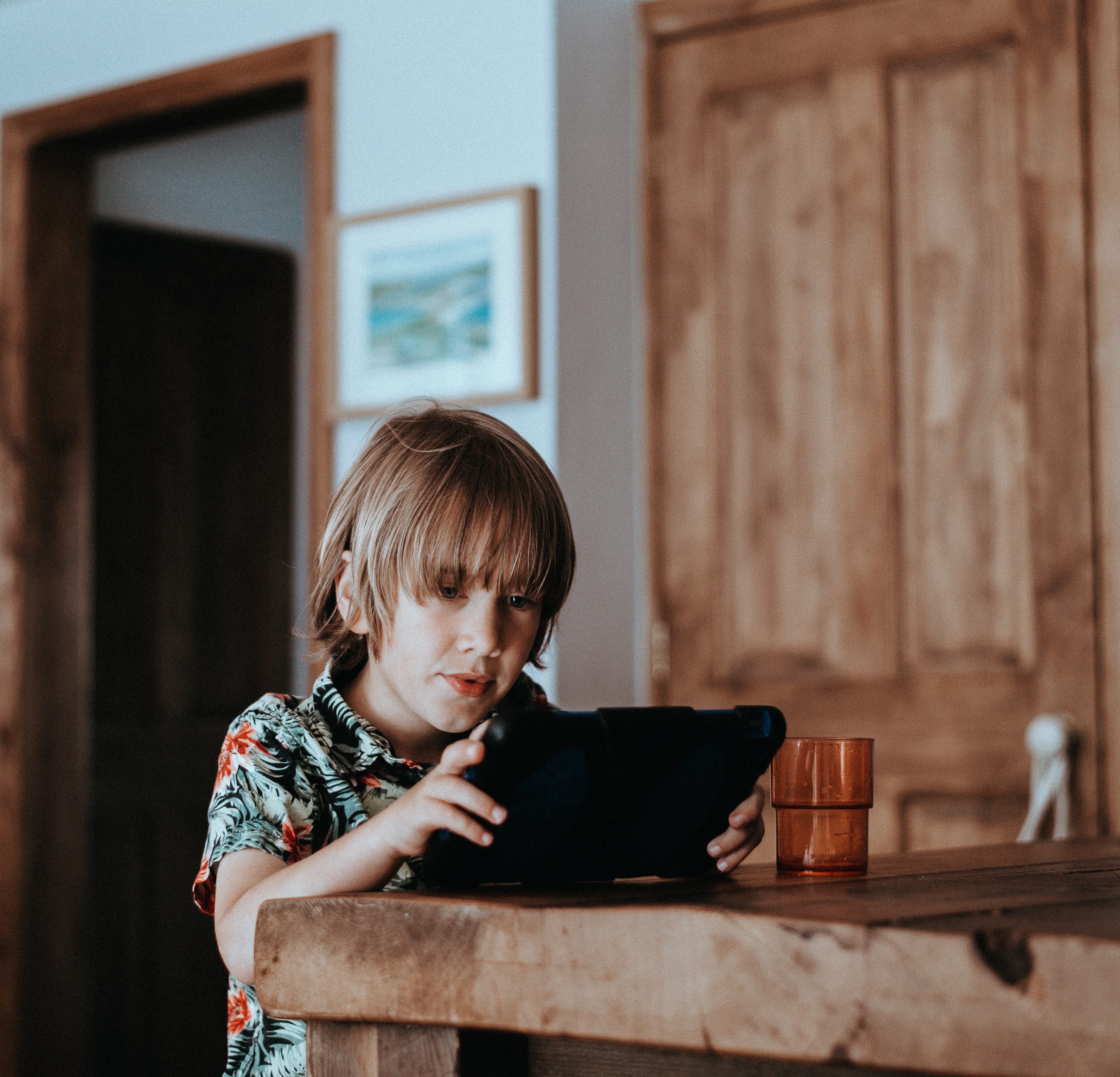 Boy playing on an iPad at a wooden table HD Wallpaper