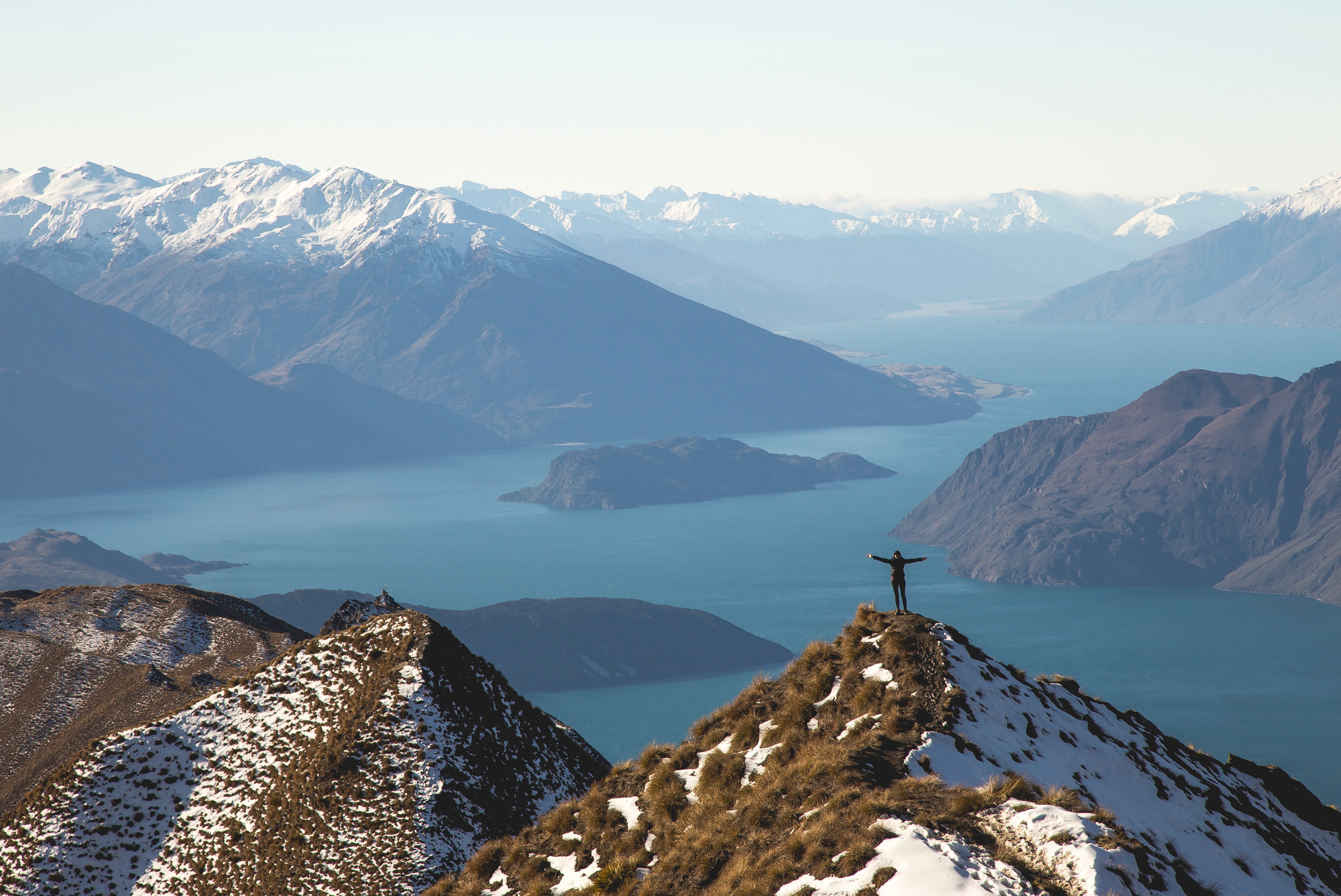 Person on snowy mountain peak overlooking Wanaka lake HD Wallpaper