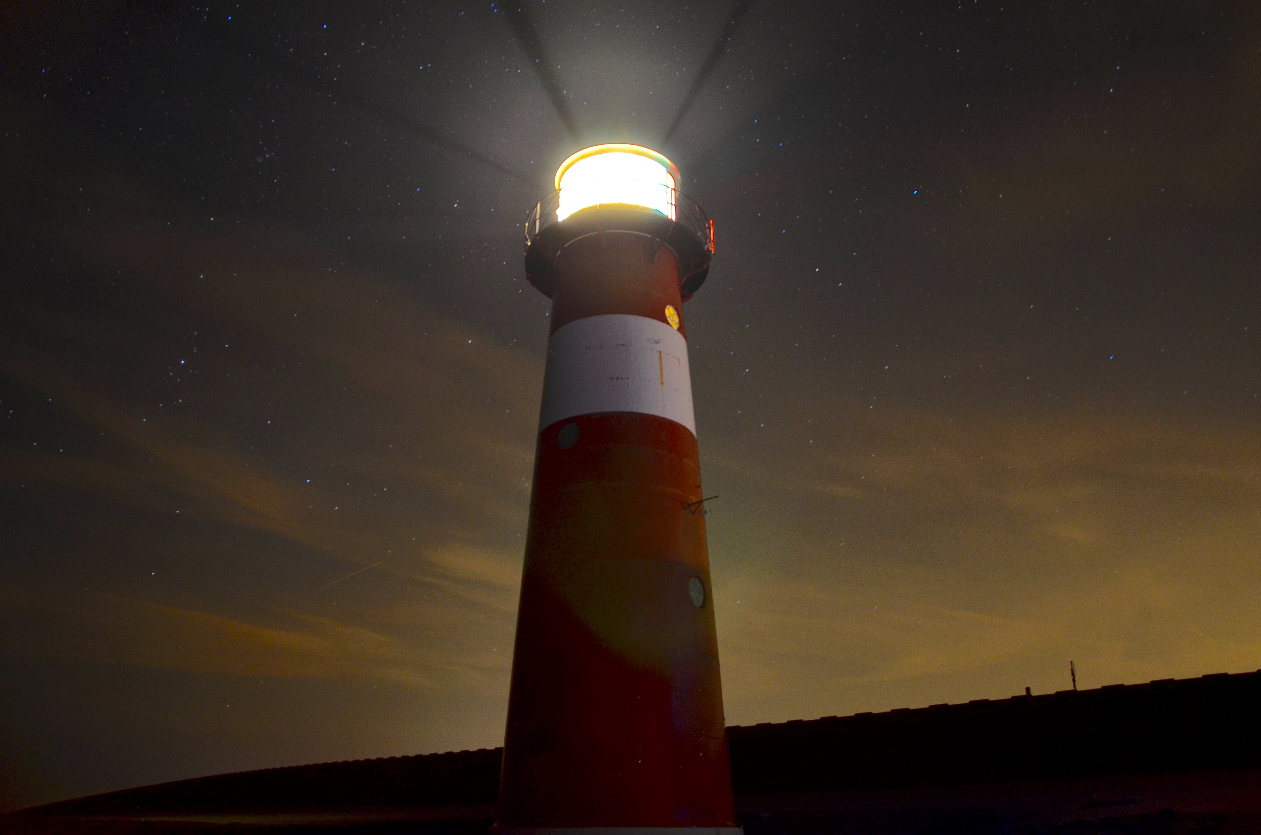 Lighthouse shining light at night with stars HD Wallpaper