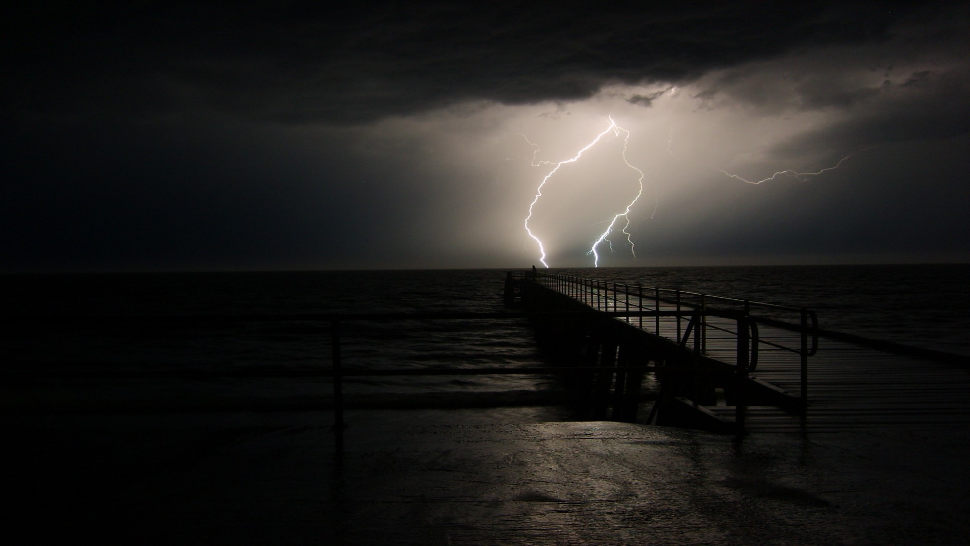 Lightning strikes over a pier at sea during a storm HD Wallpaper