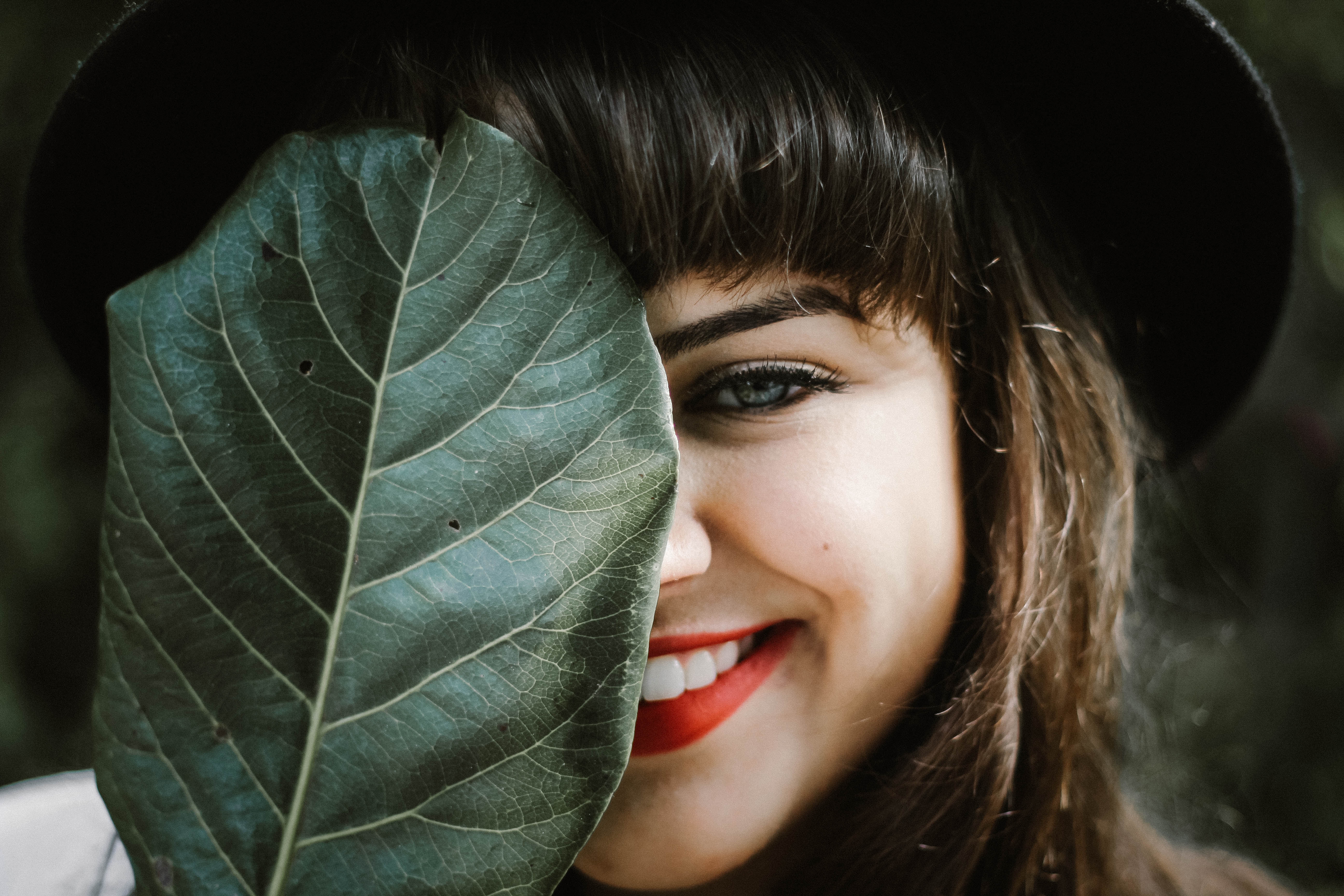 Woman in hat hiding face with a large green leaf HD Wallpaper