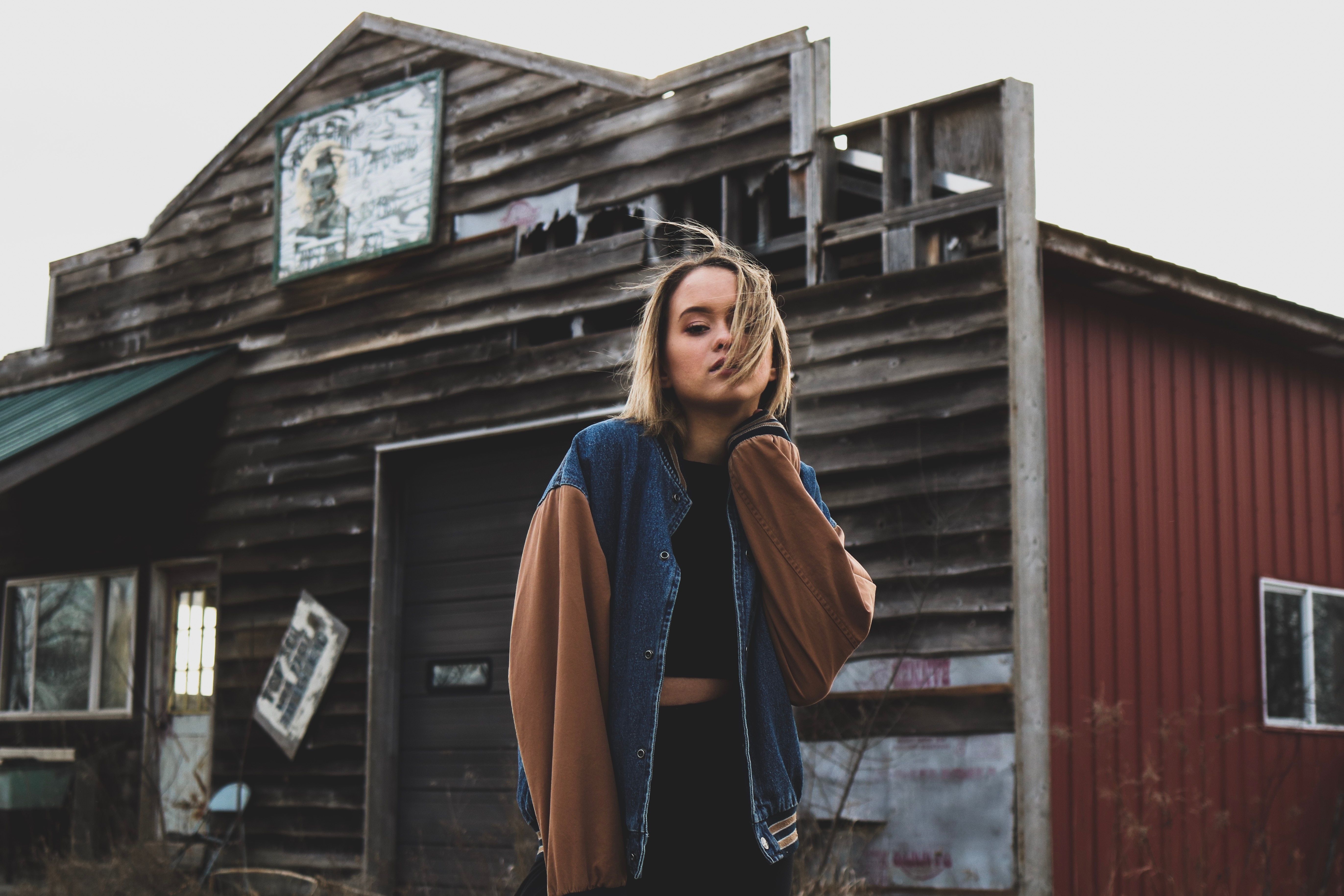 Woman in a denim and brown jacket outside an abandoned barn HD Wallpaper