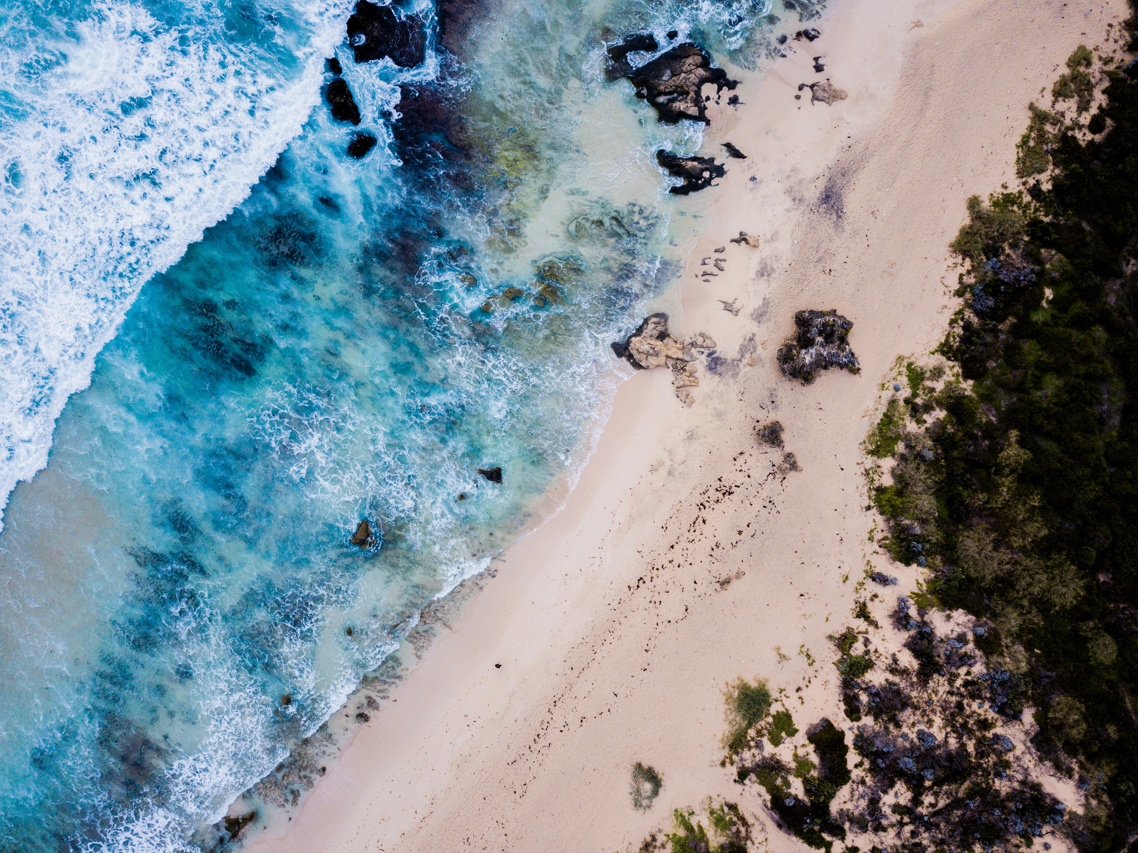 Aerial view of a rocky beach with turquoise ocean waves HD Wallpaper