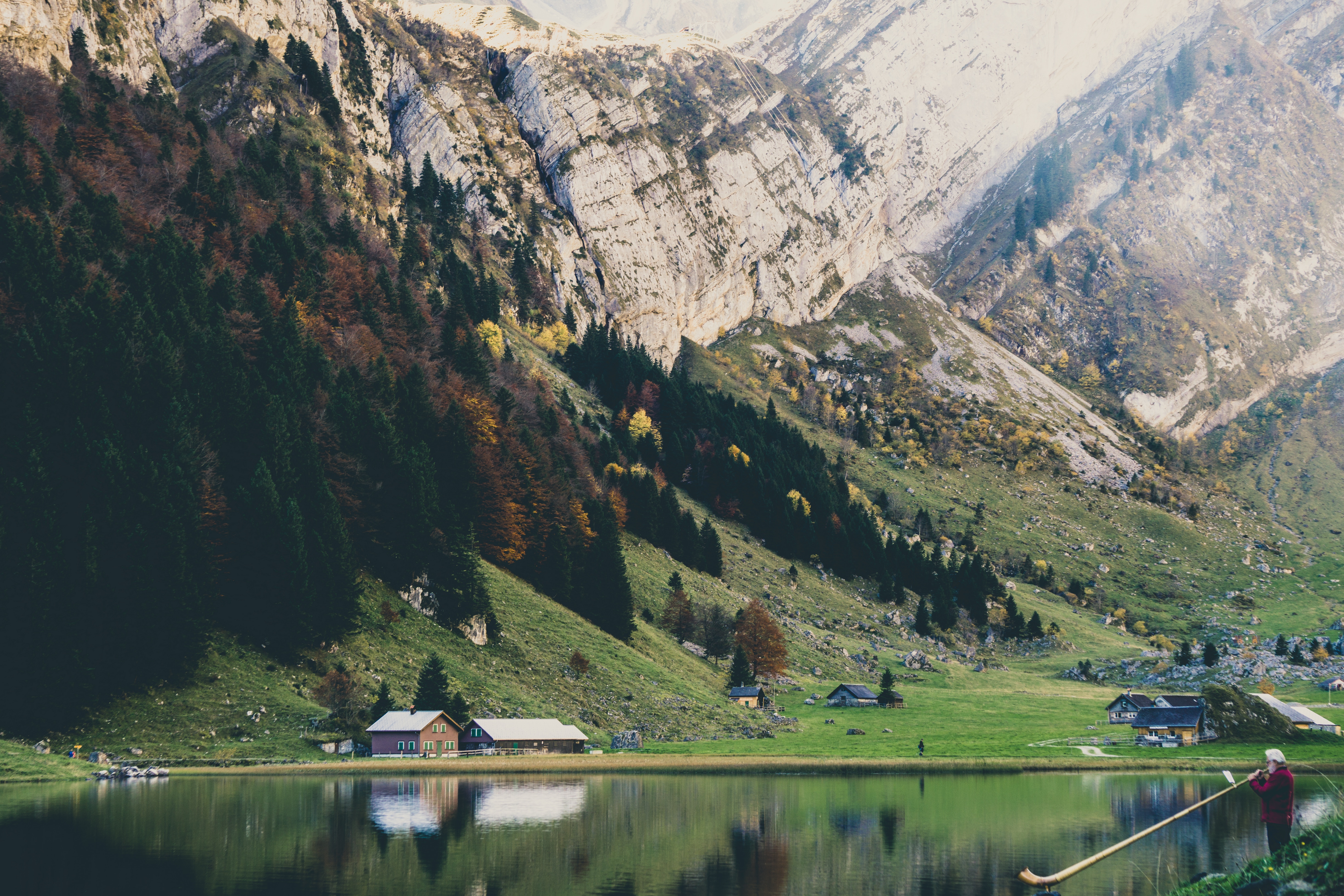 Man plays alphorn by a lake in the Swiss Alps HD Wallpaper