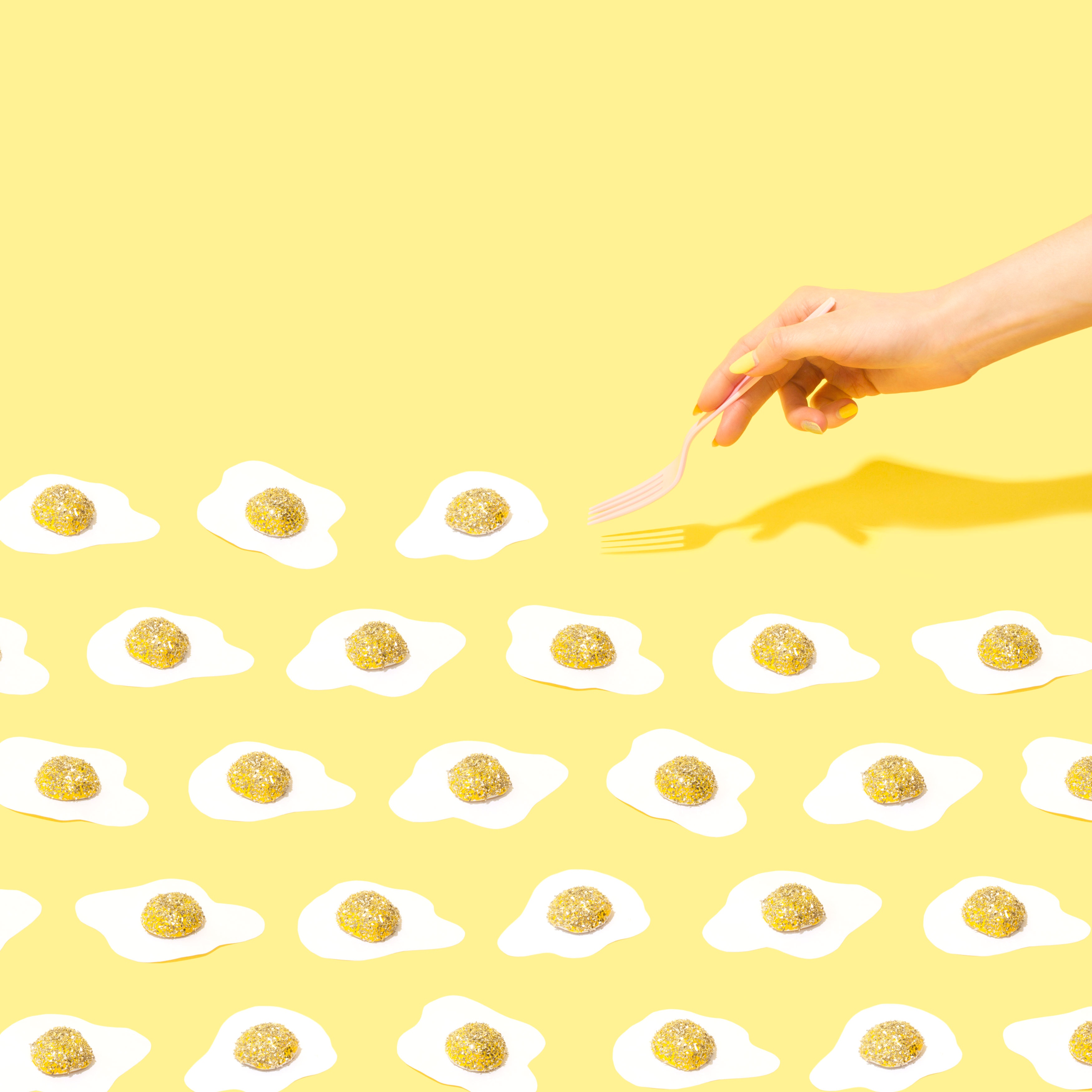Hand with fork reaching for glittery egg candies on yellow background HD Wallpaper