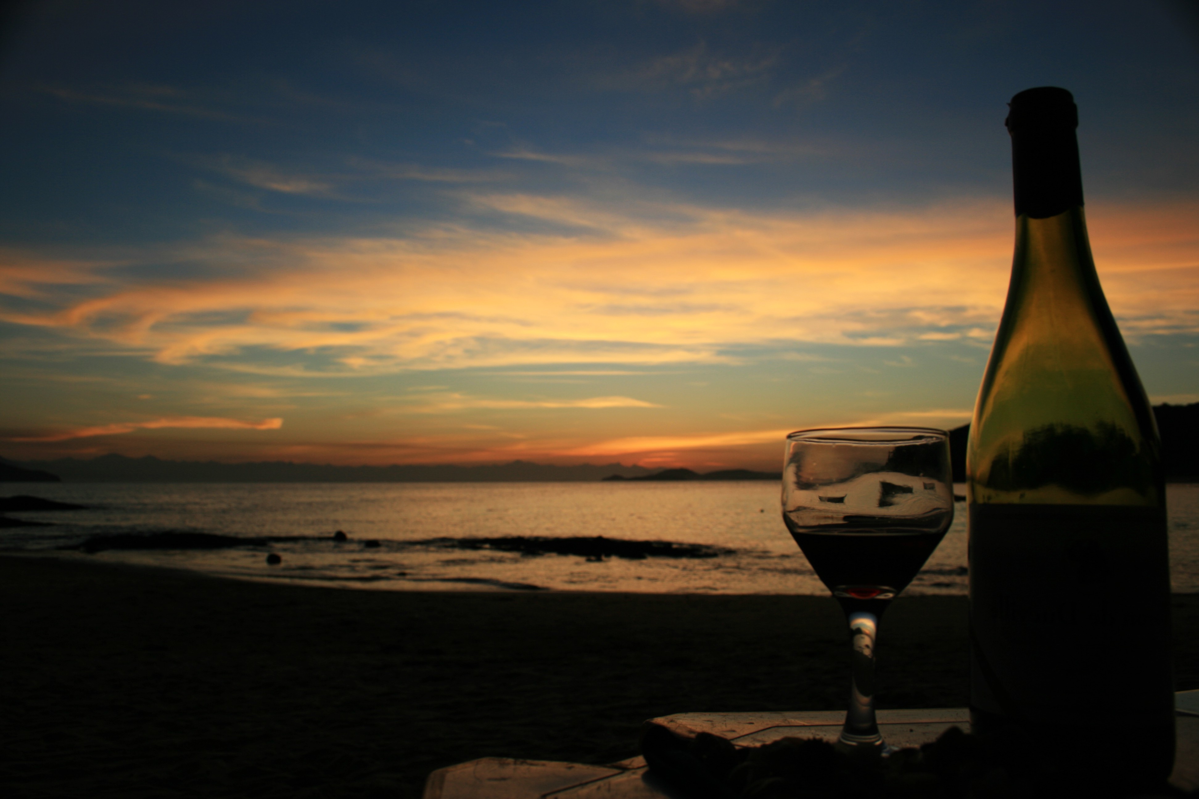 Wine bottle and glass on beach at sunset HD Wallpaper