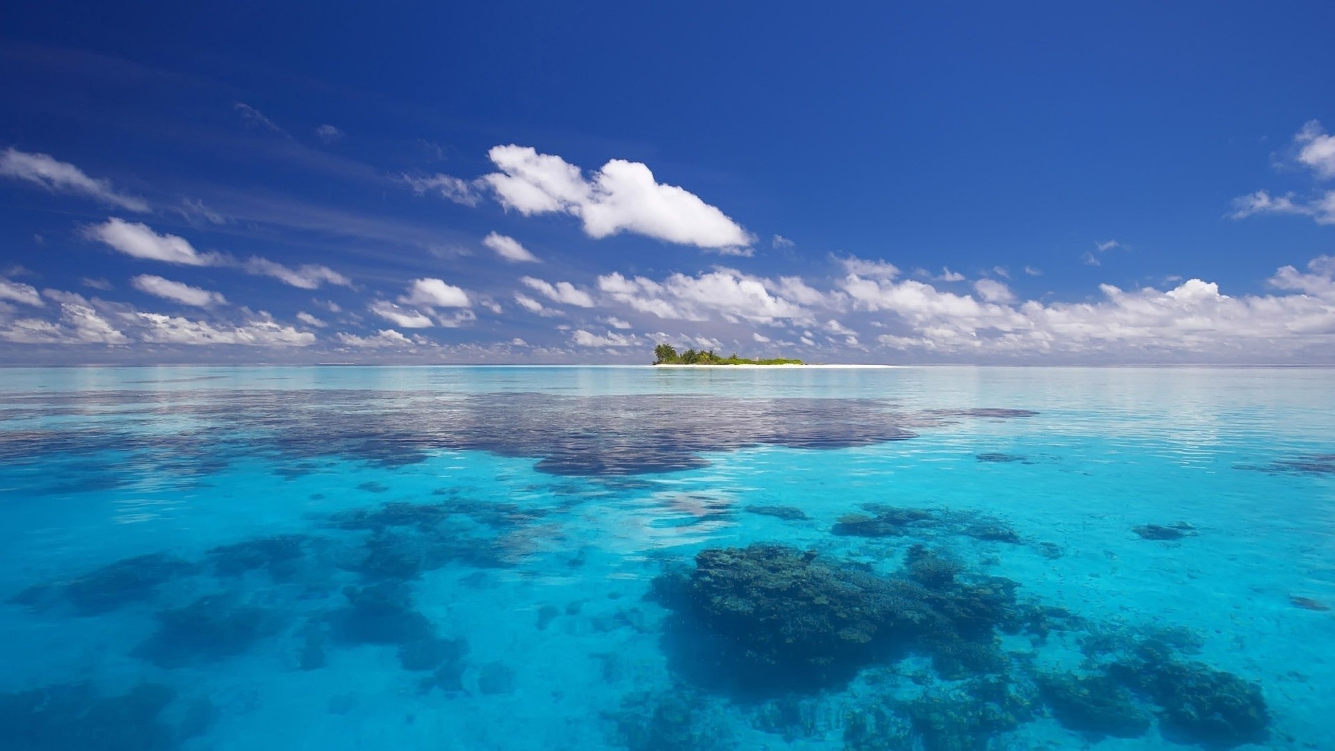 Tropical island in a clear blue ocean under a cloudy sky HD Wallpaper