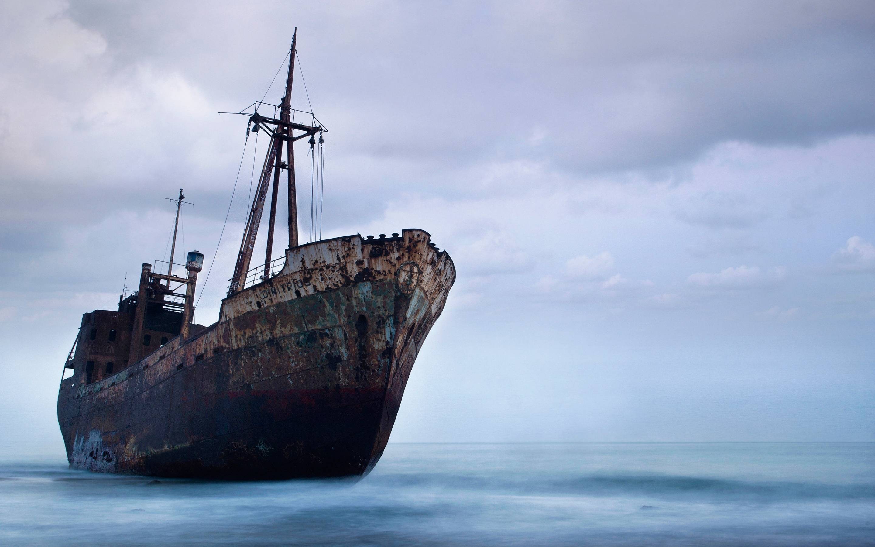Rusty shipwreck on a beach under a cloudy sky HD Wallpaper