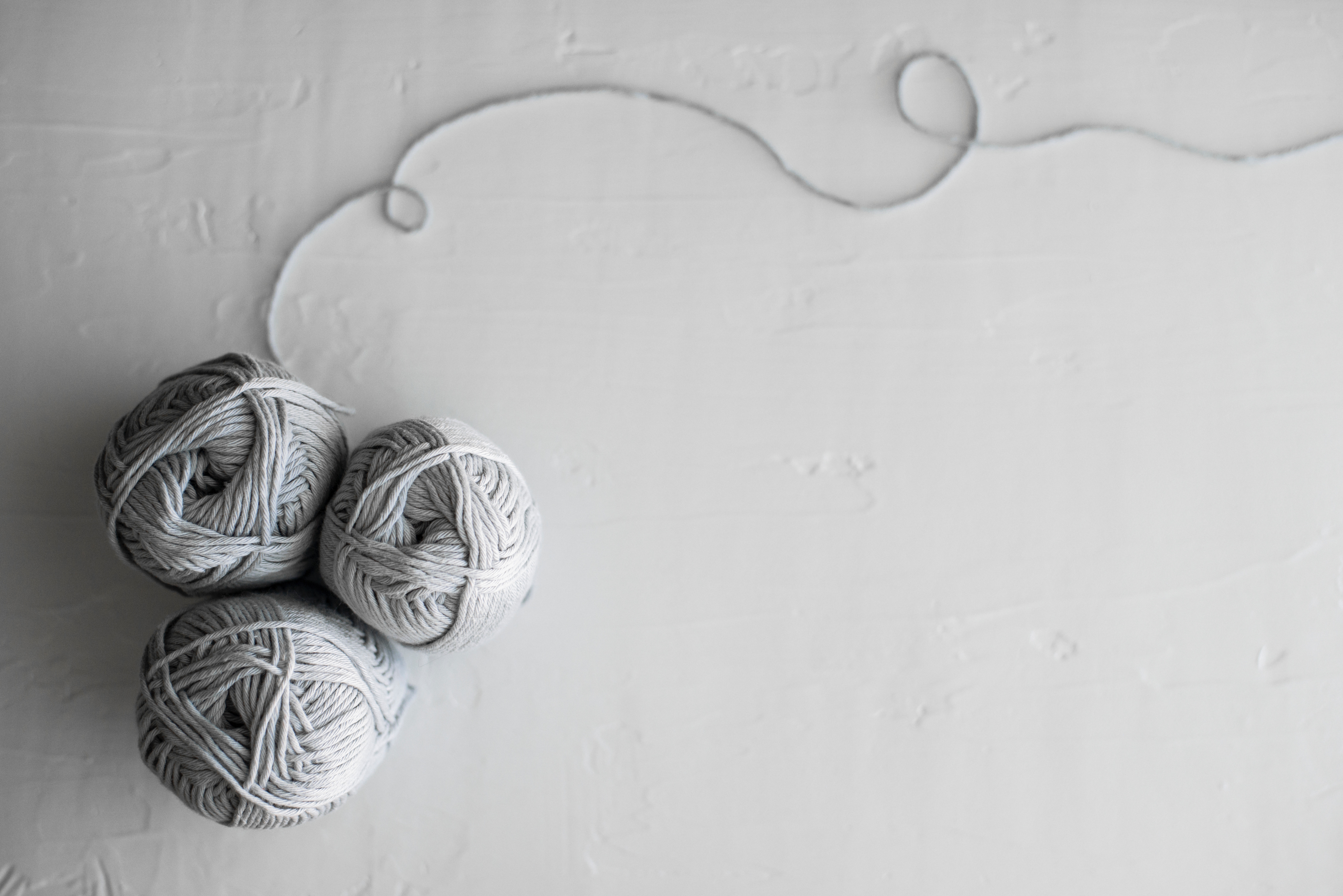 Three balls of gray yarn with a strand of yarn HD Wallpaper
