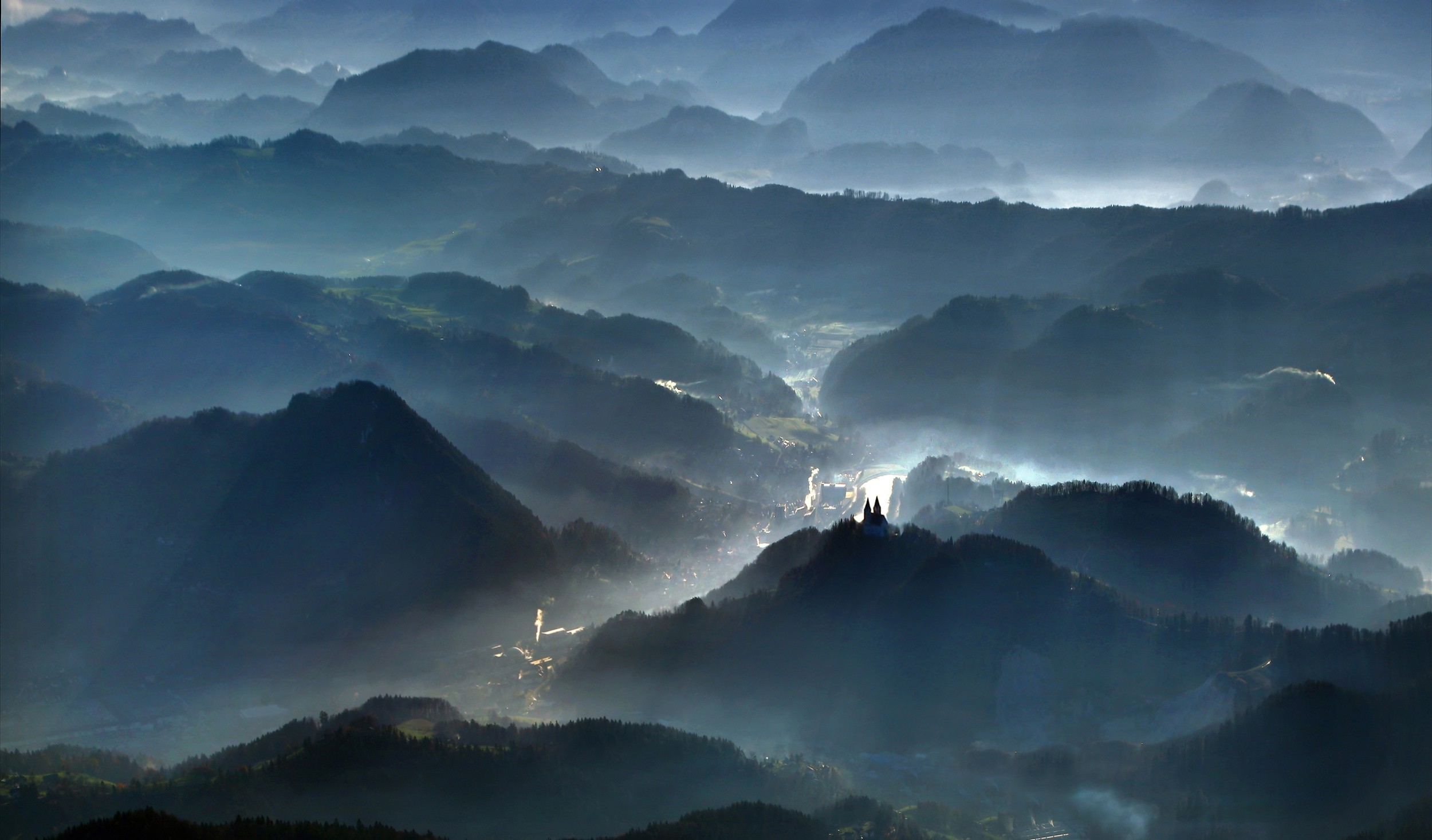 Misty blue mountains with a village in the valley HD Wallpaper