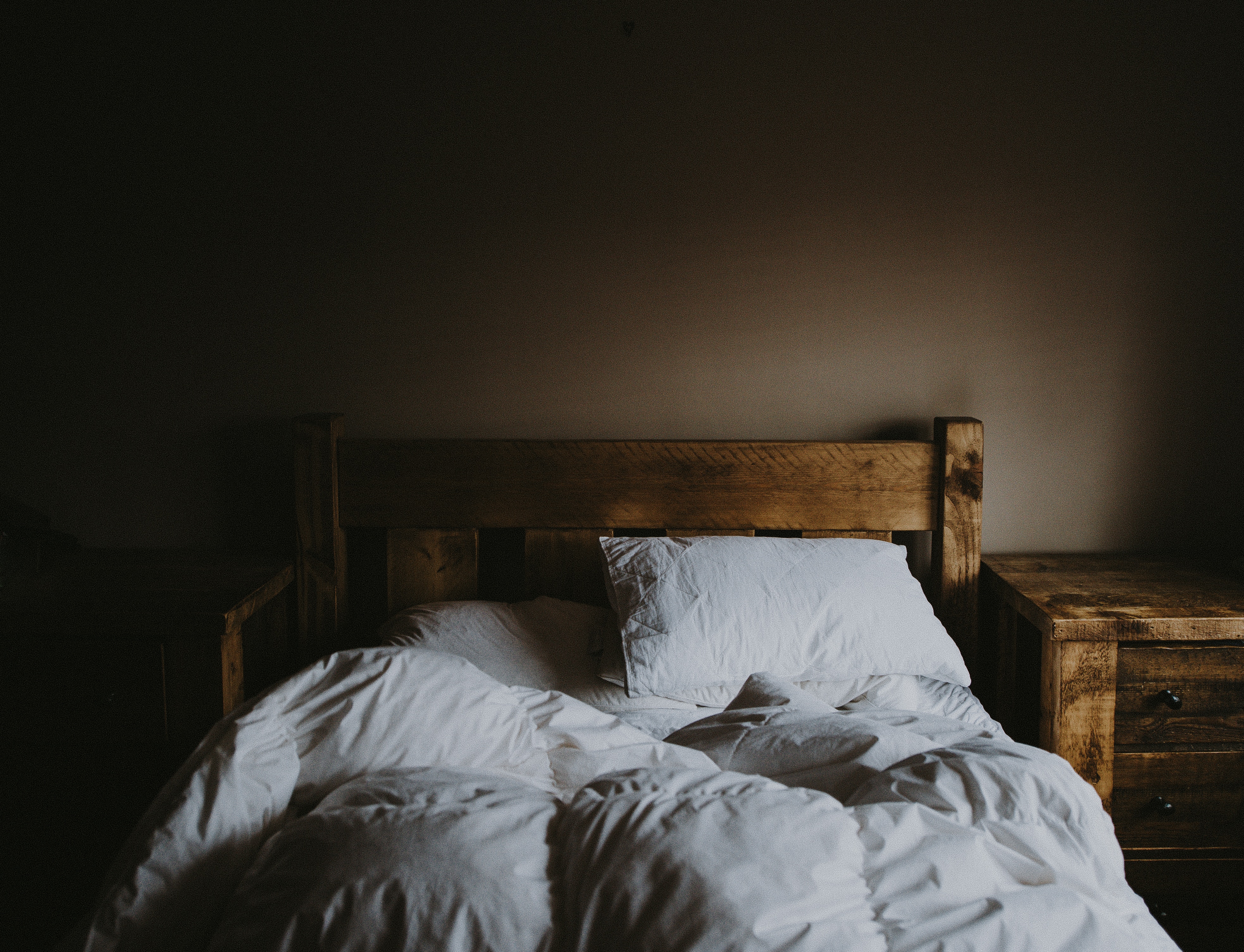 Wooden bed with white bedding and pillows in a dark room HD Wallpaper
