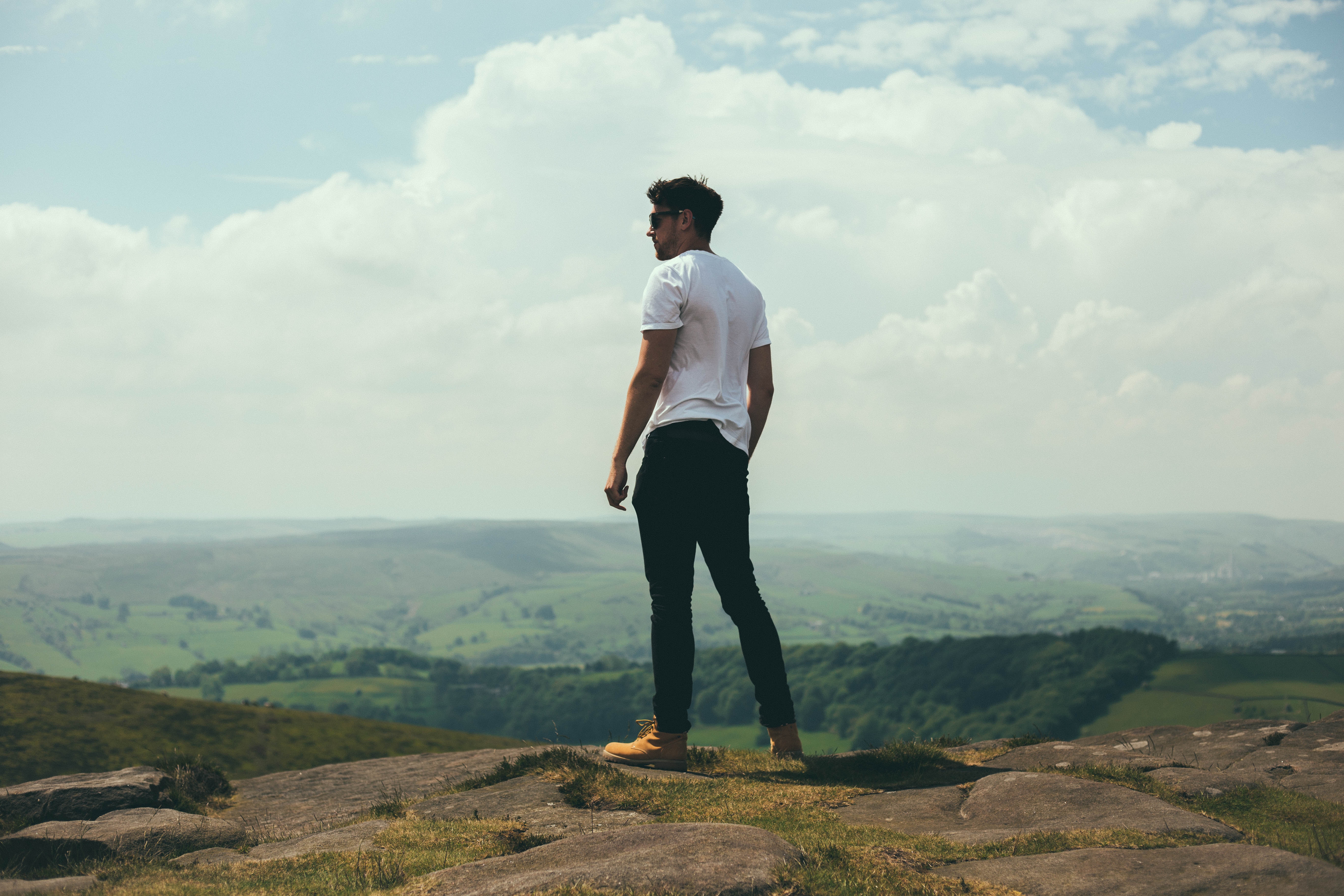 Man on a rocky outcrop overlooking a green valley HD Wallpaper