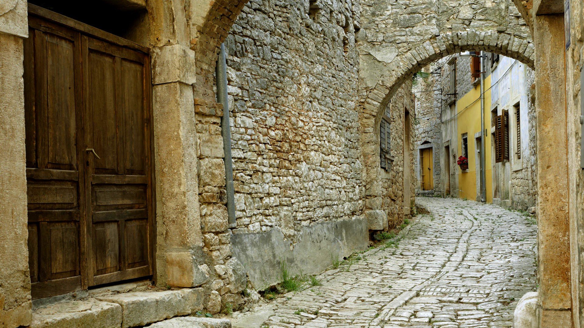 Old stone street with arched passage and wooden door HD Wallpaper