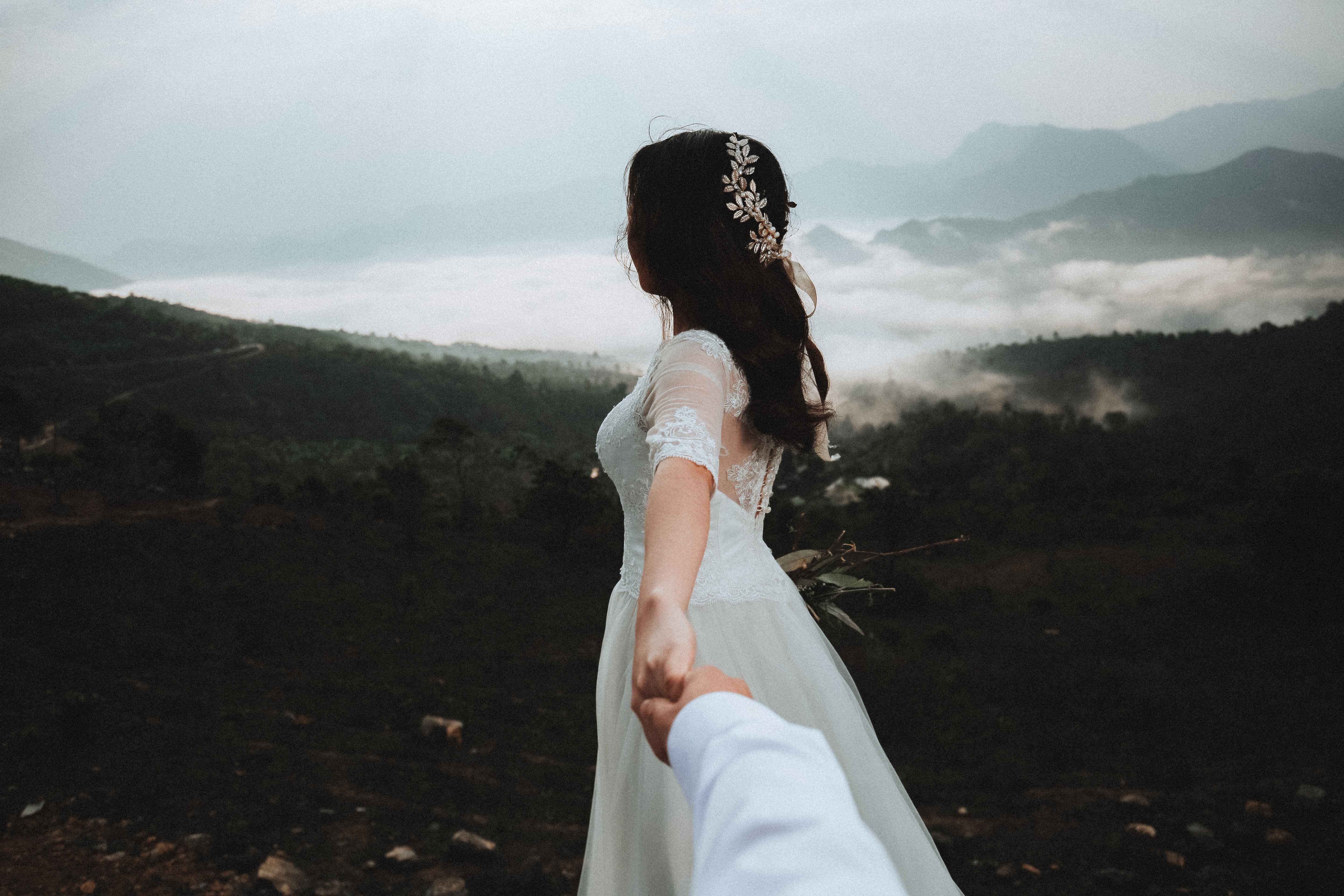 Bride in wedding dress holding hands in misty mountains HD Wallpaper
