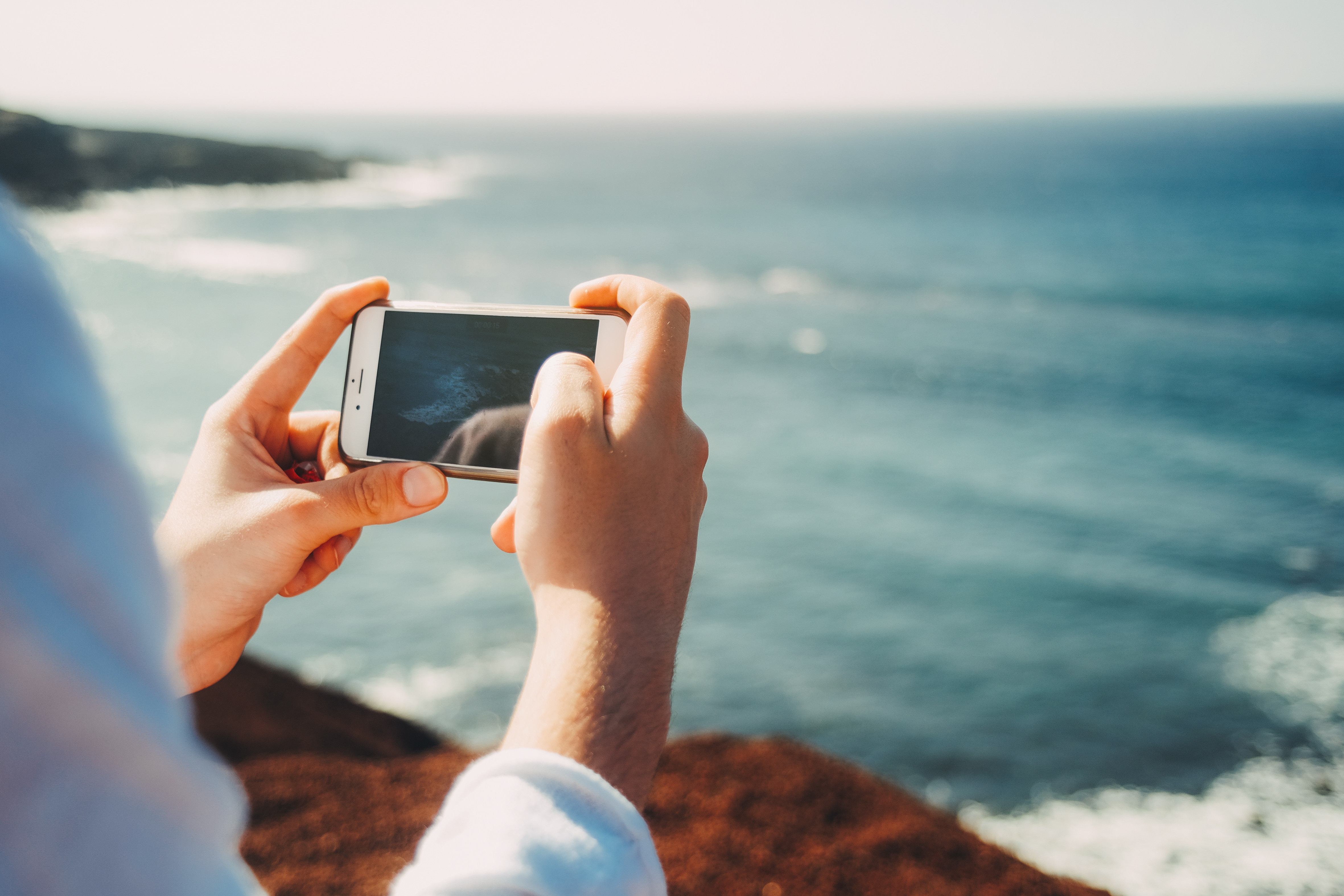 Person holding iPhone to capture ocean view HD Wallpaper