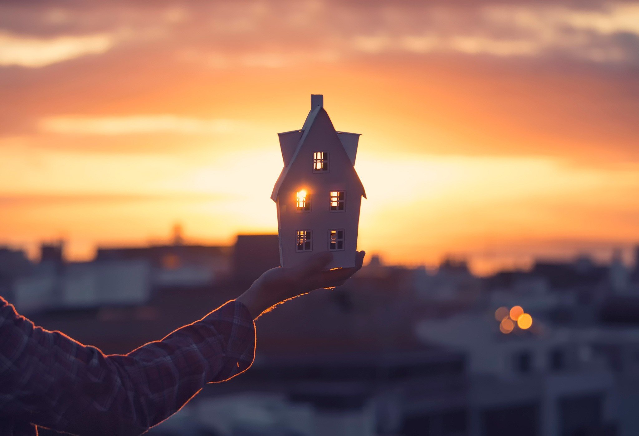 Hand holding a model house at sunset HD Wallpaper