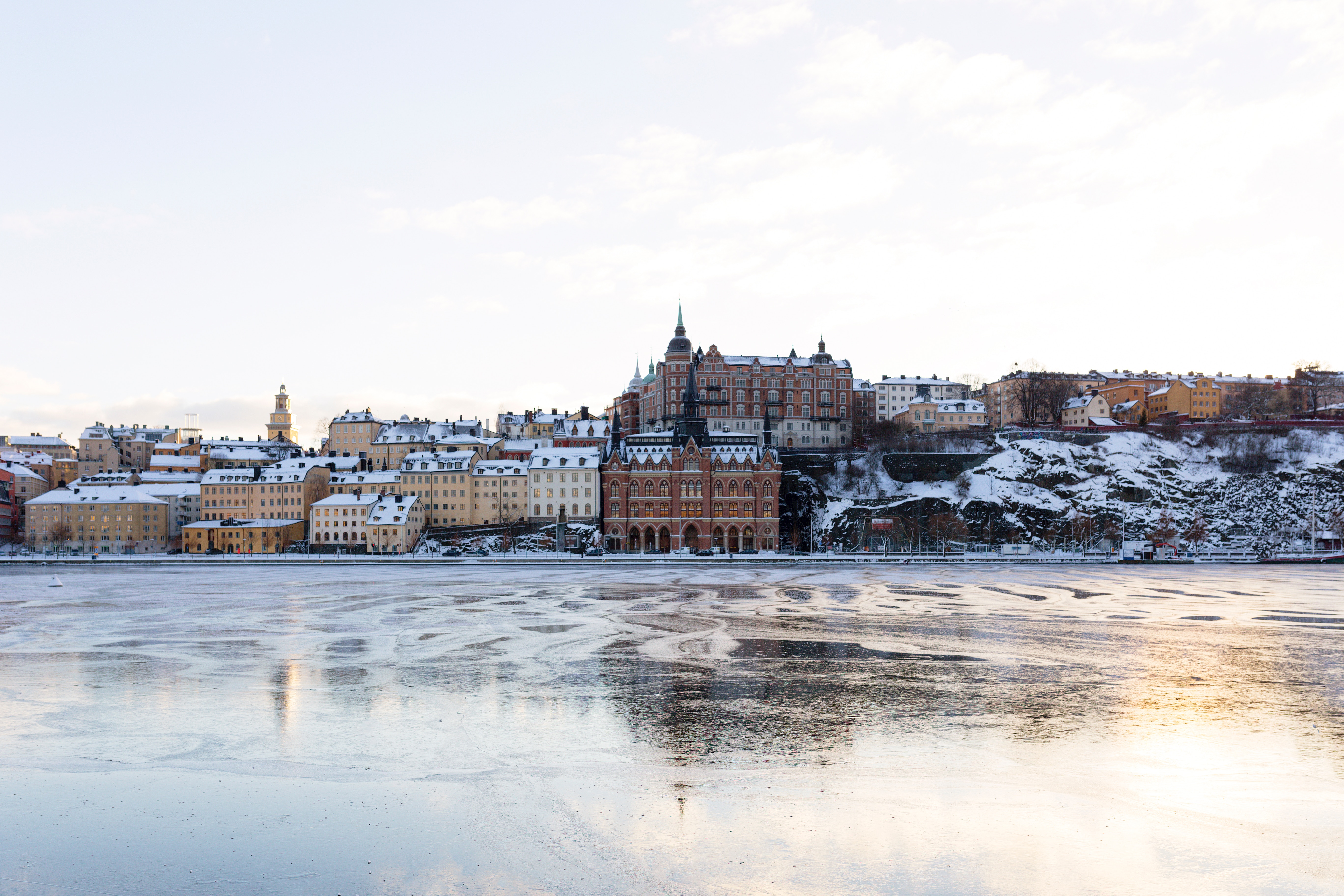 Stockholm waterfront with snow-covered buildings and icy river HD Wallpaper
