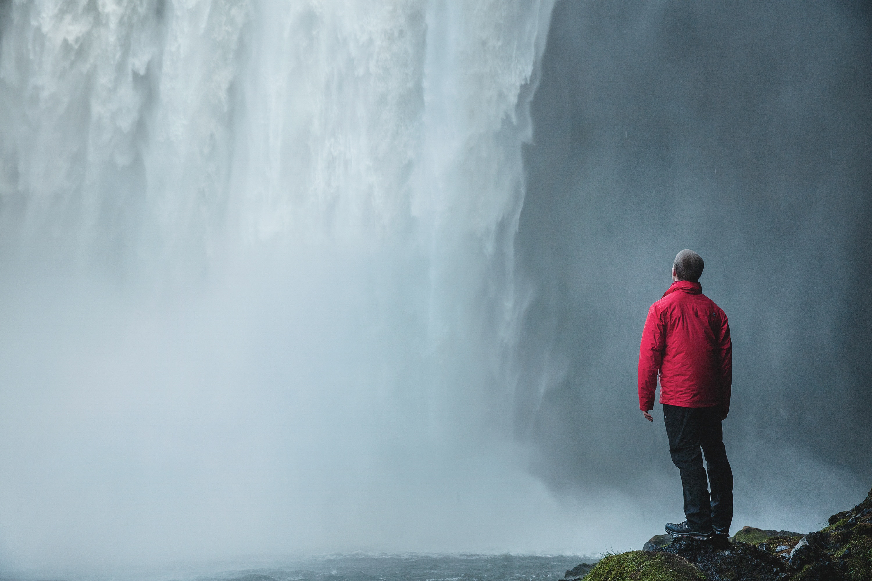 Man in red jacket standing by a waterfall HD Wallpaper