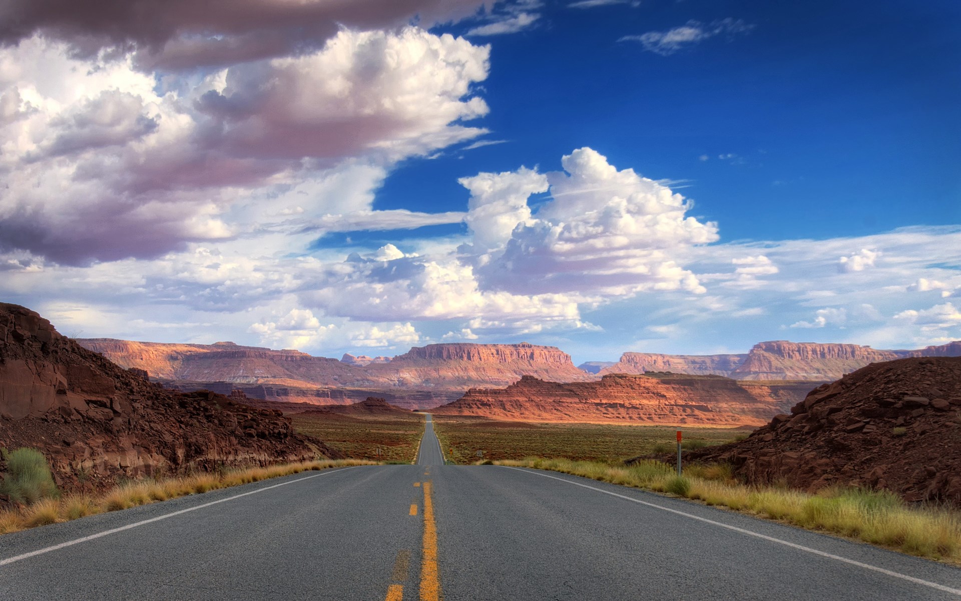 Desert highway leading to mesas under a cloudy sky HD Wallpaper