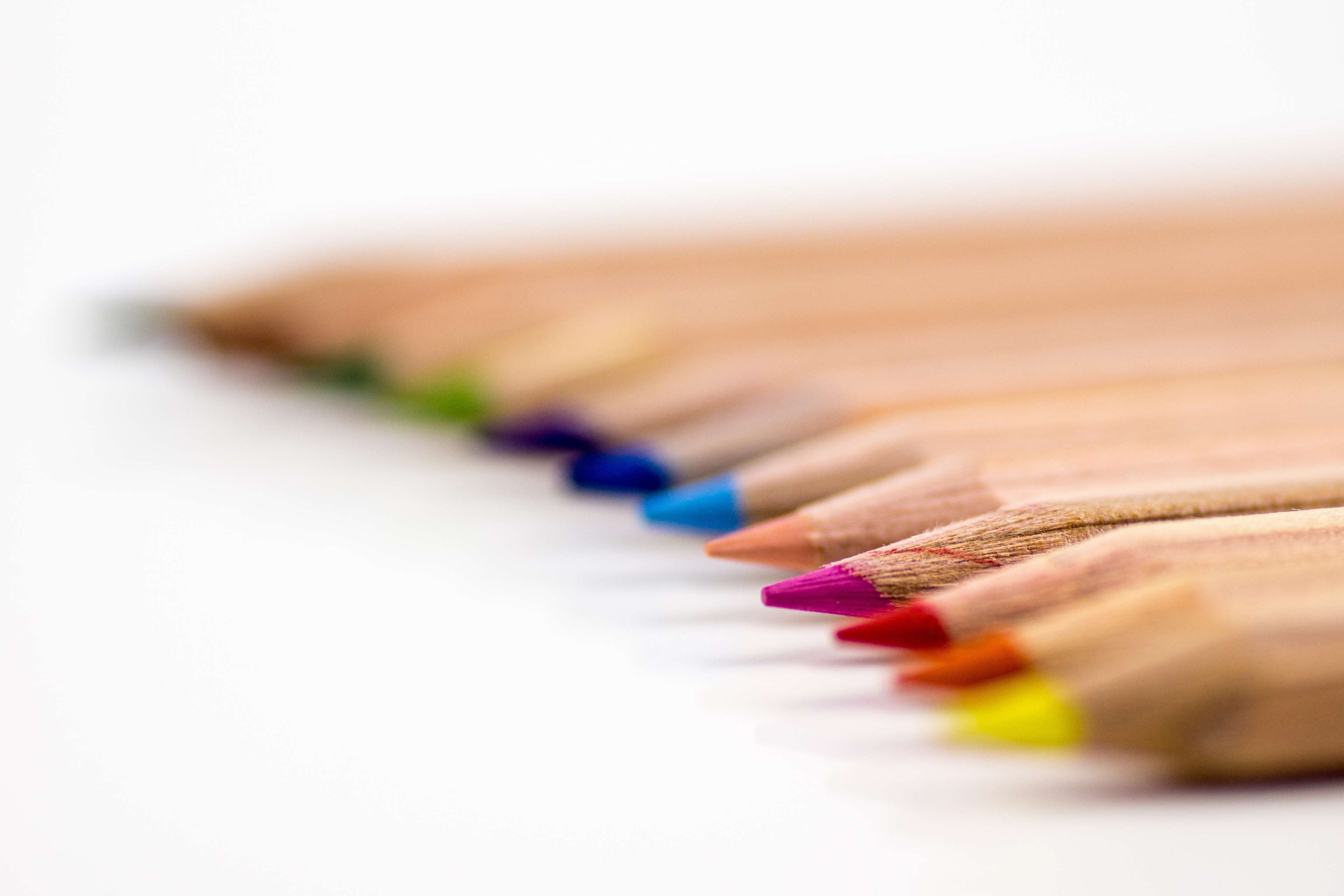 Colored pencils arranged in a row on a white surface HD Wallpaper