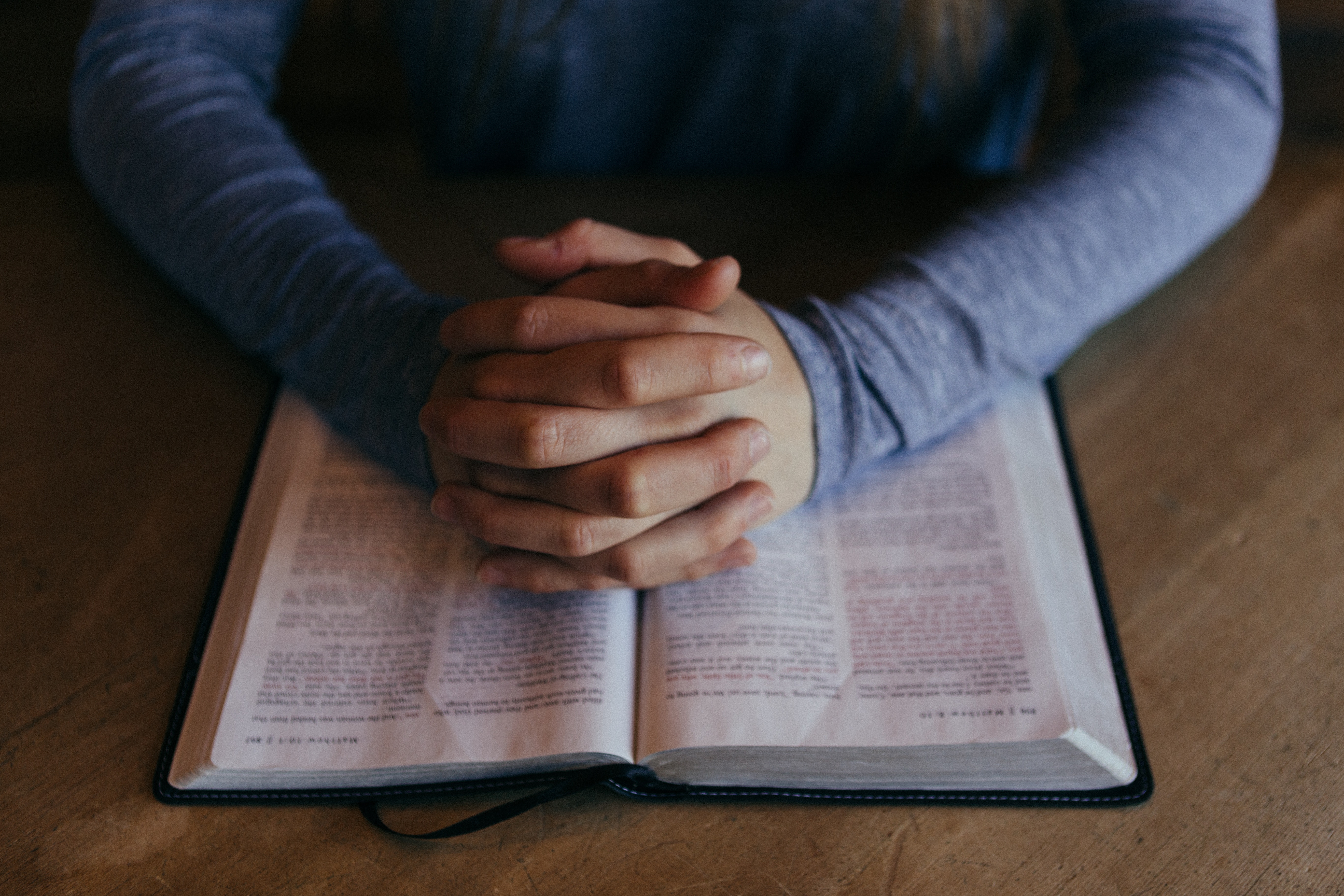 Person praying with hands folded over a Bible HD Wallpaper