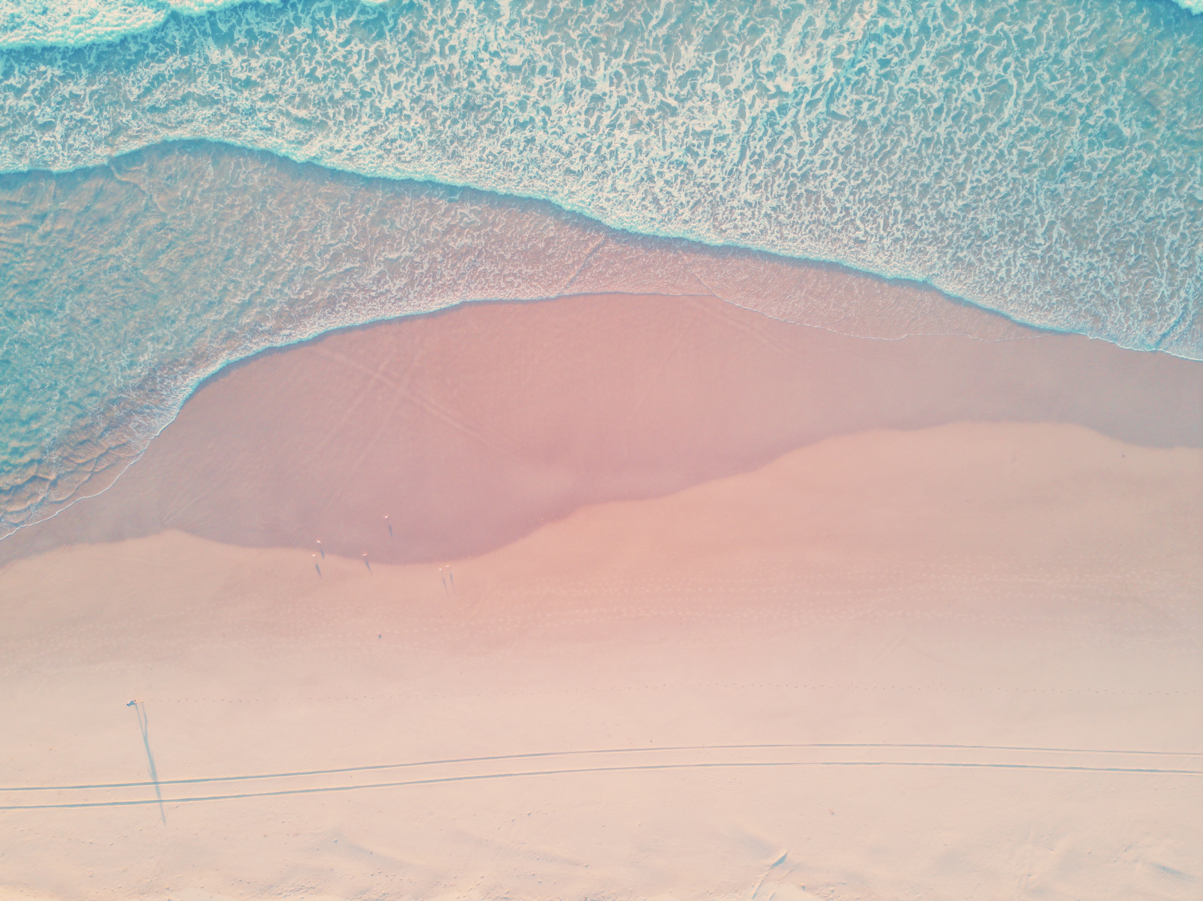Aerial view of a pink sand beach with blue ocean waves HD Wallpaper
