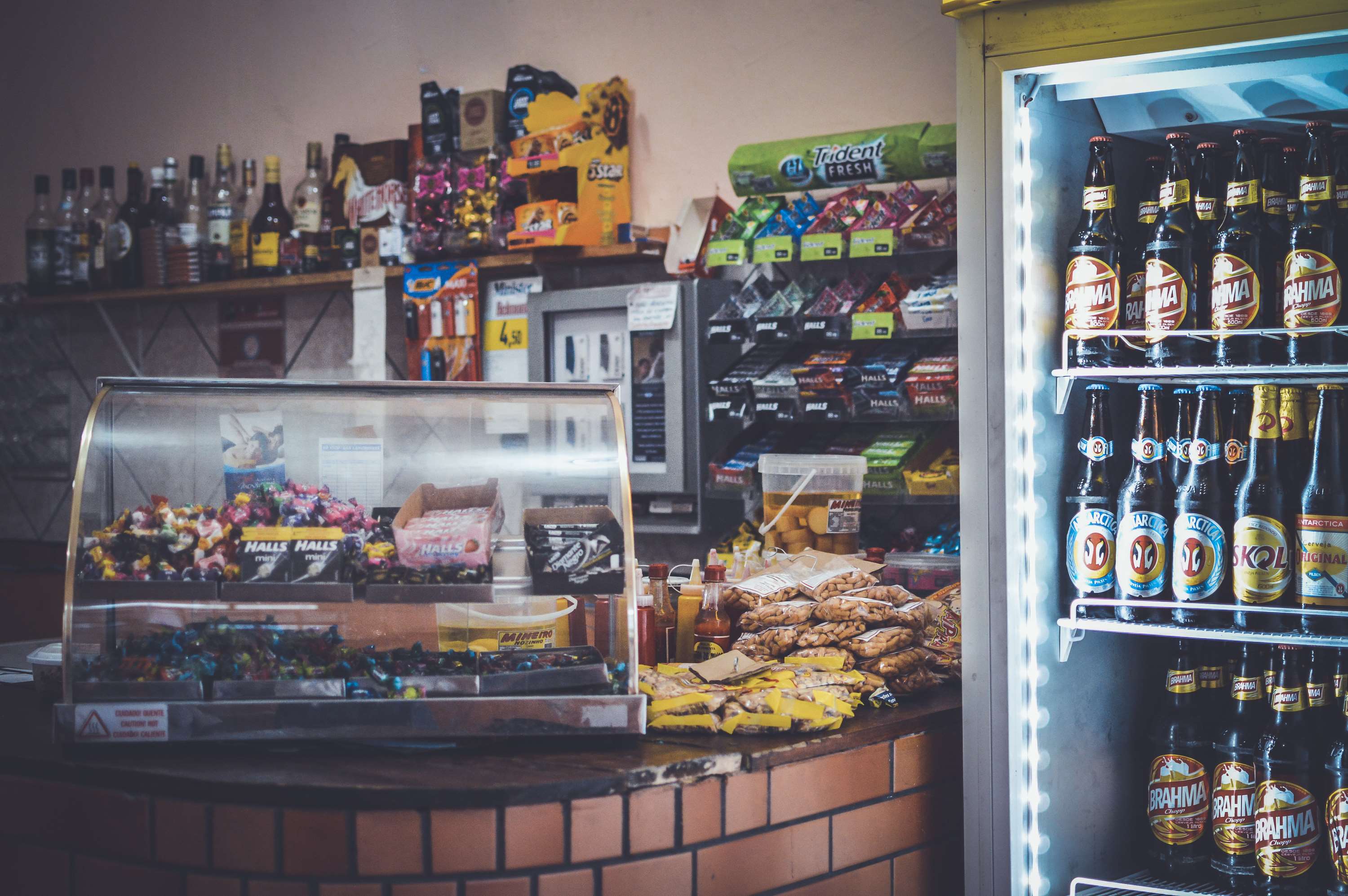 Corner store counter with candy, snacks, and refrigerated beers HD Wallpaper