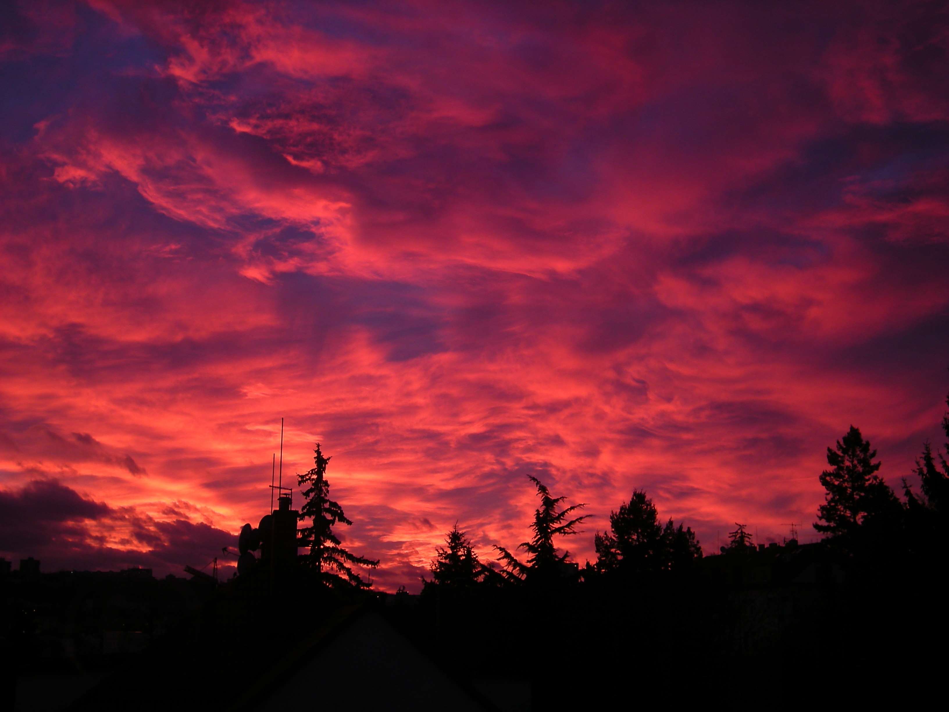 Dramatic sunset sky over silhouetted trees and buildings HD Wallpaper