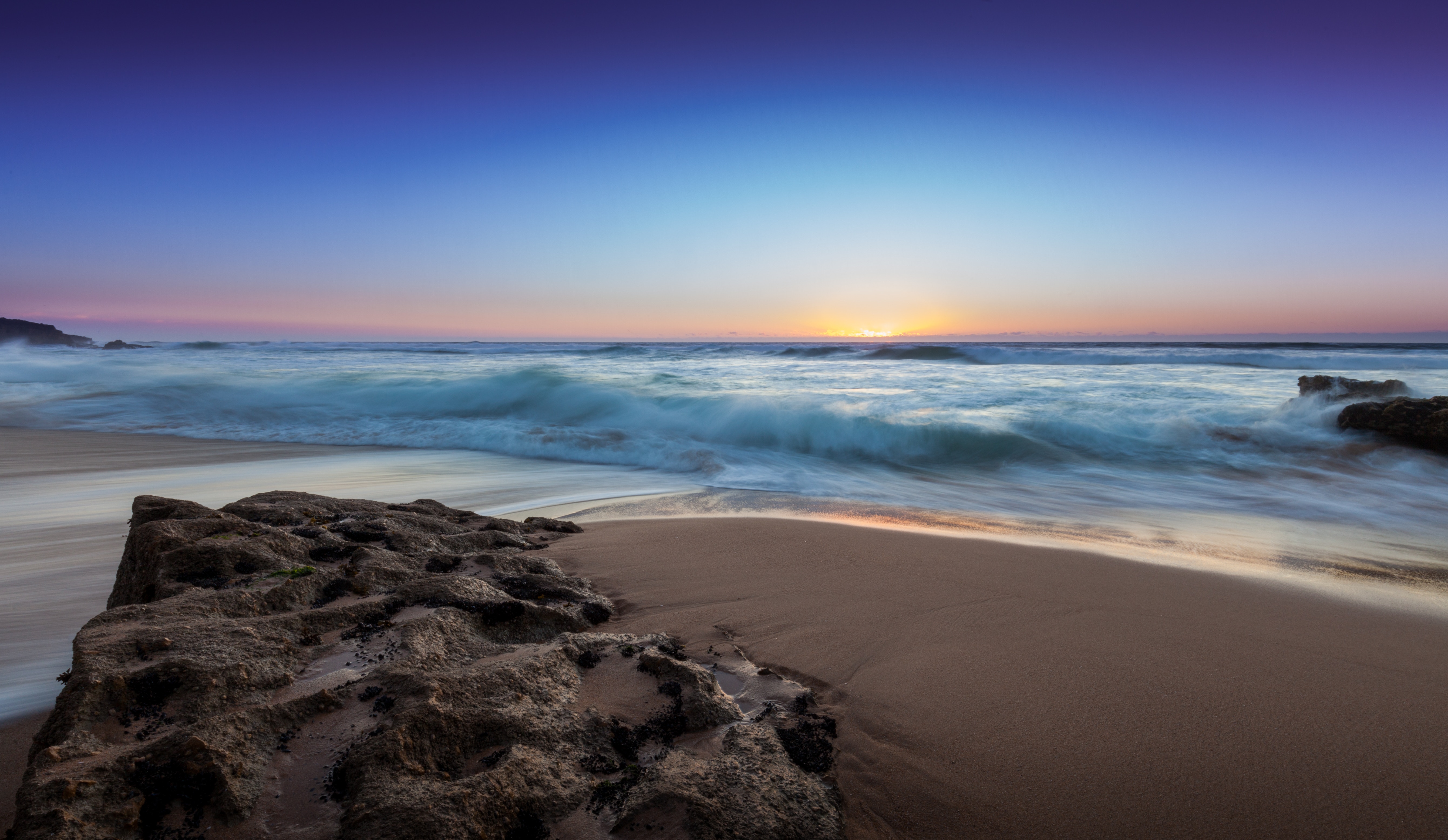 Long exposure of waves crashing on a beach at sunset HD Wallpaper