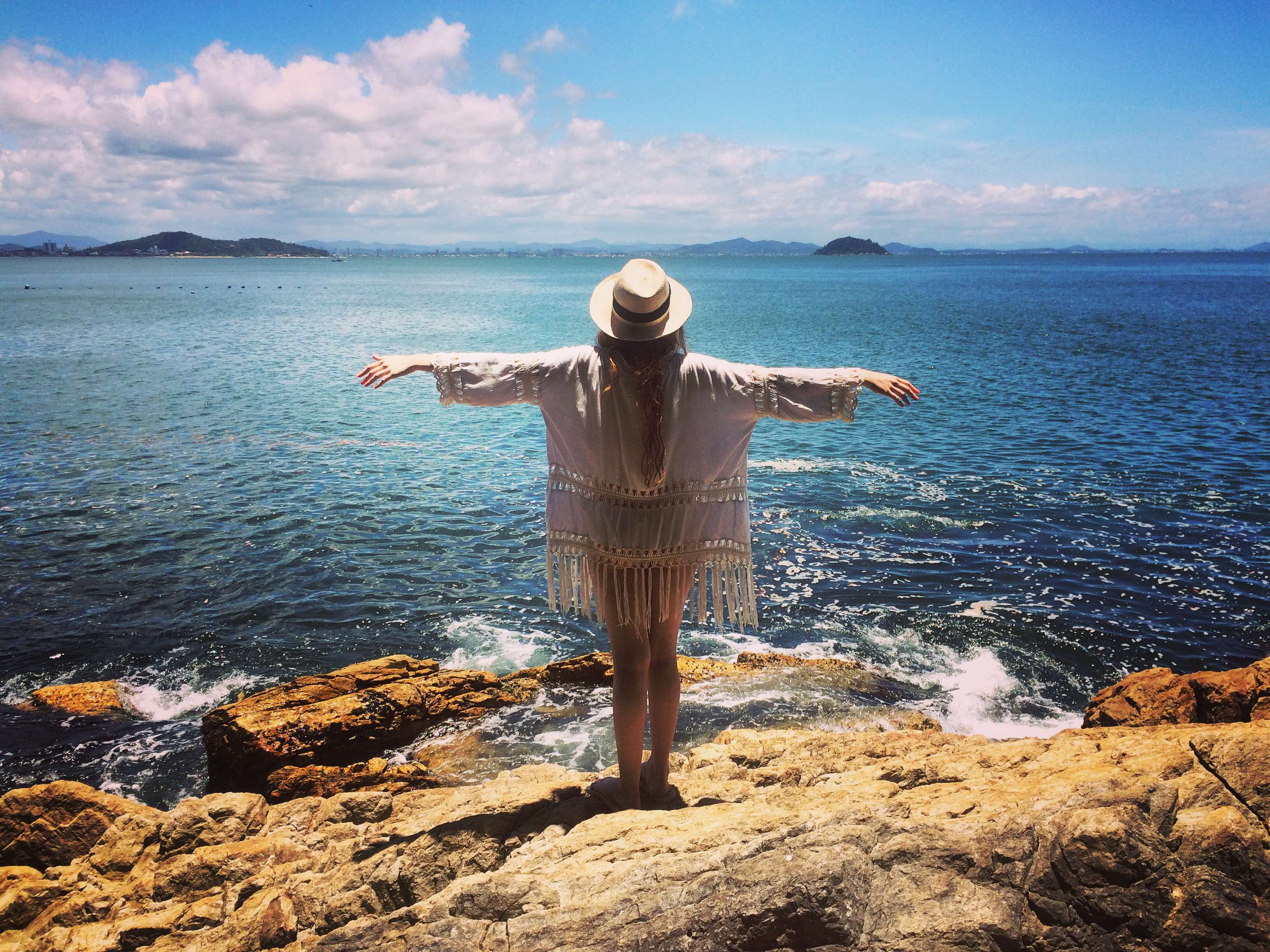 Woman in white cover-up and hat on rocky shore HD Wallpaper