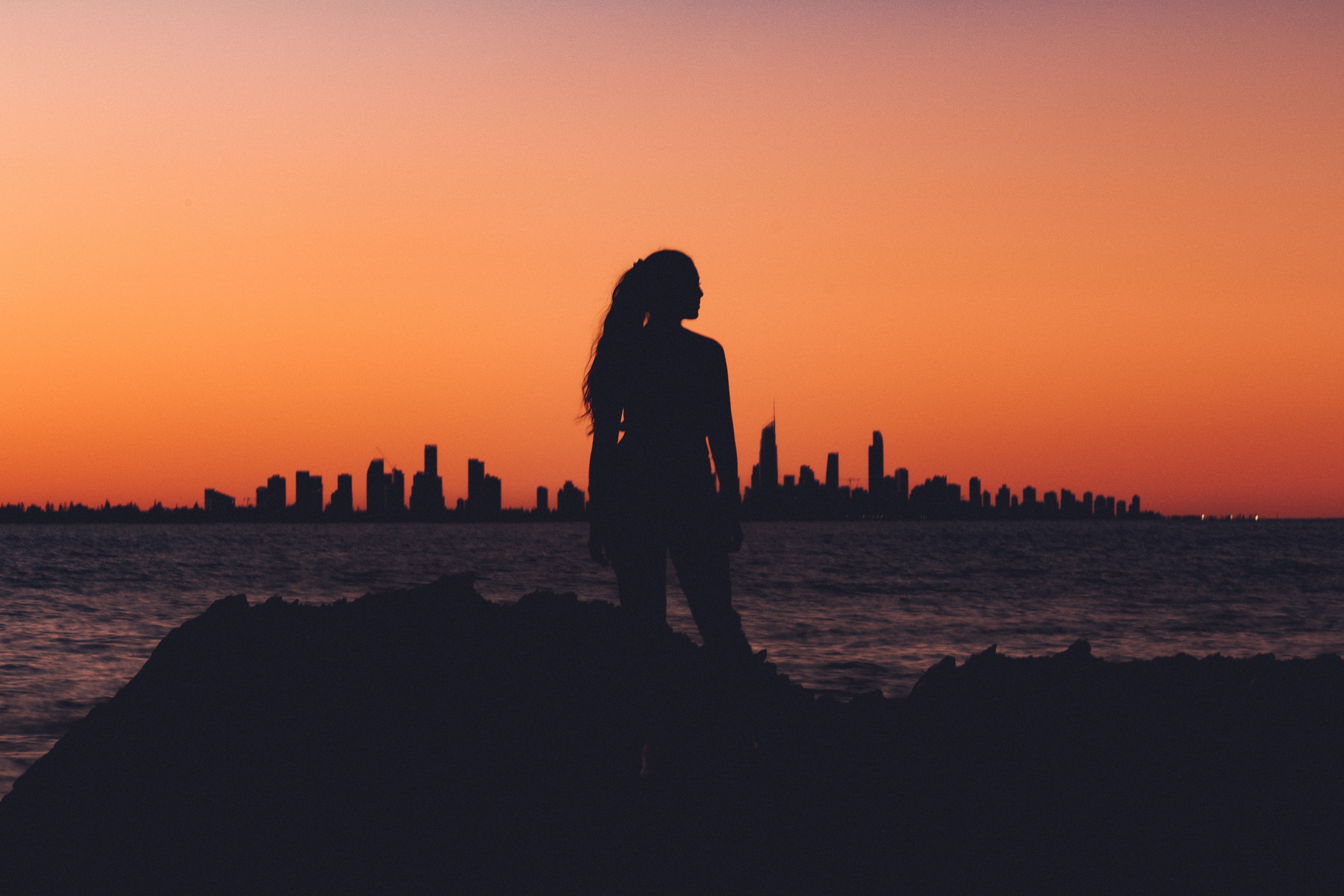 Silhouette of a woman watching a city skyline at sunset HD Wallpaper