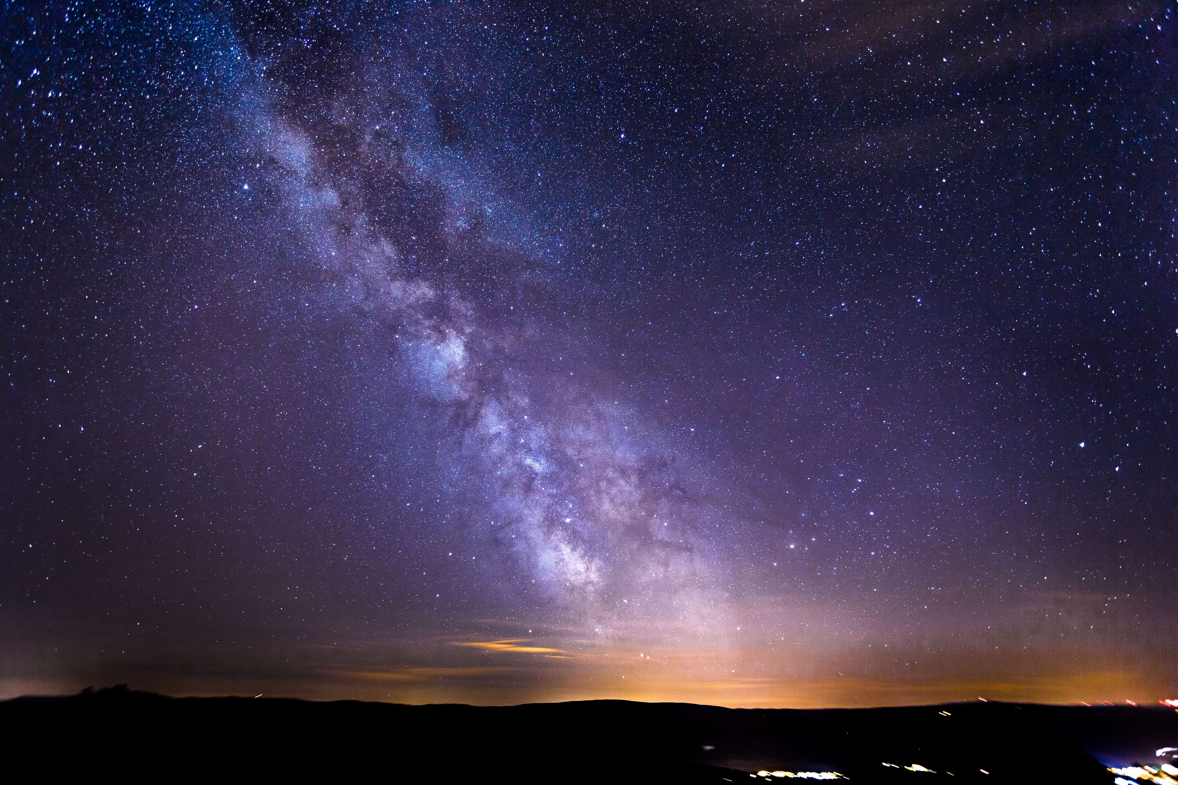 Milky Way over a dark landscape with distant city lights HD Wallpaper