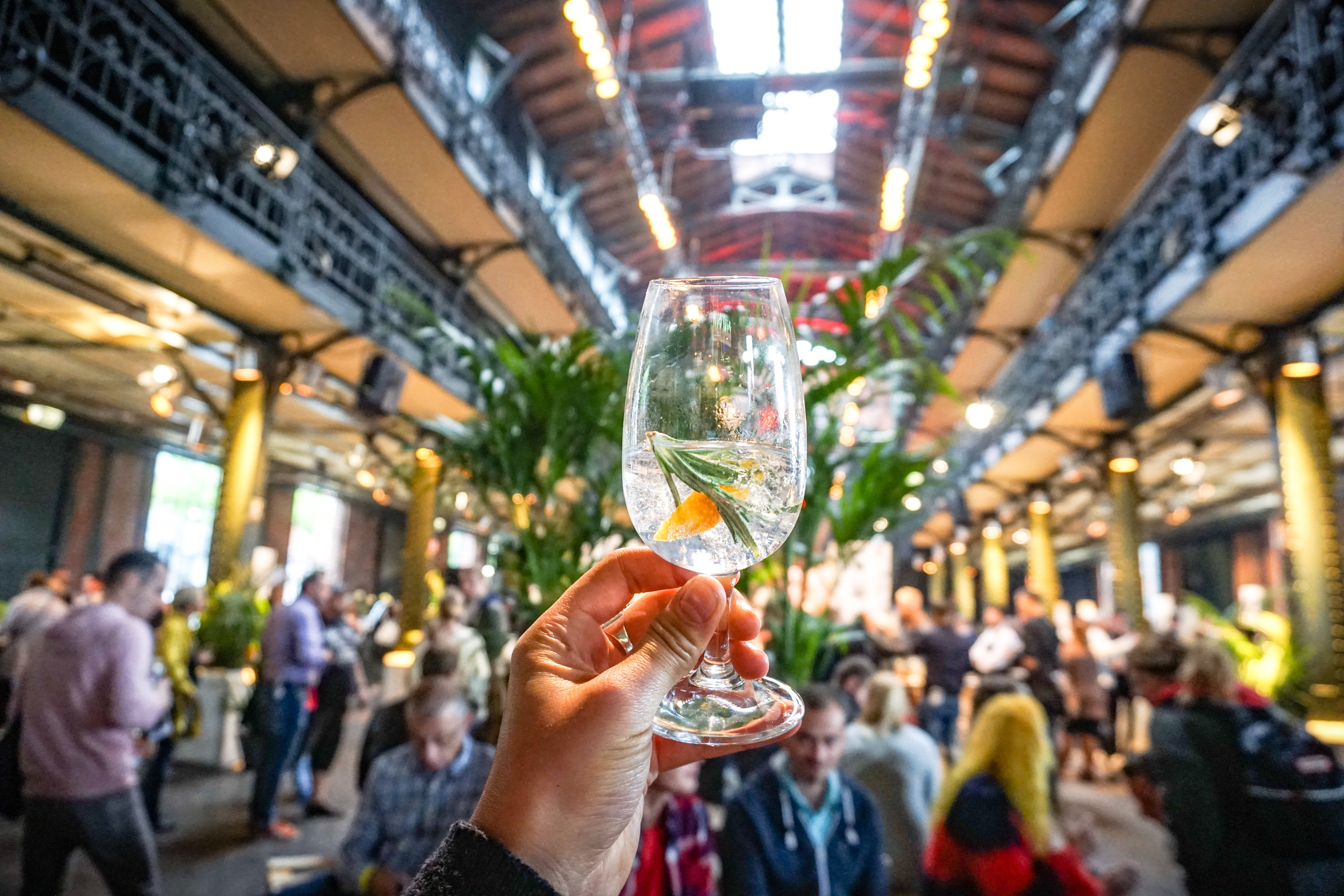 Hand holding a gin cocktail in a busy market HD Wallpaper
