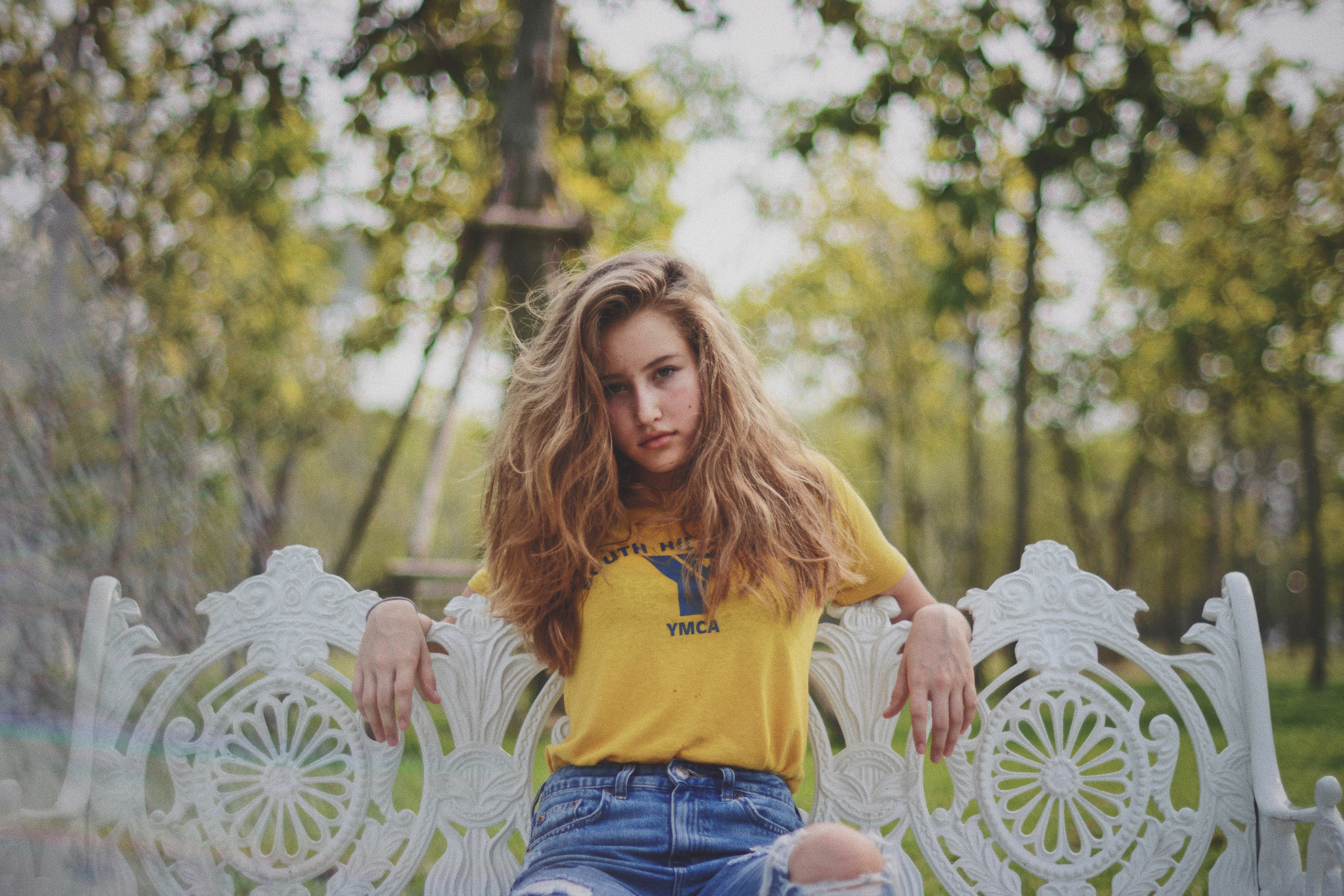 Woman in yellow YMCA shirt on ornate white bench HD Wallpaper