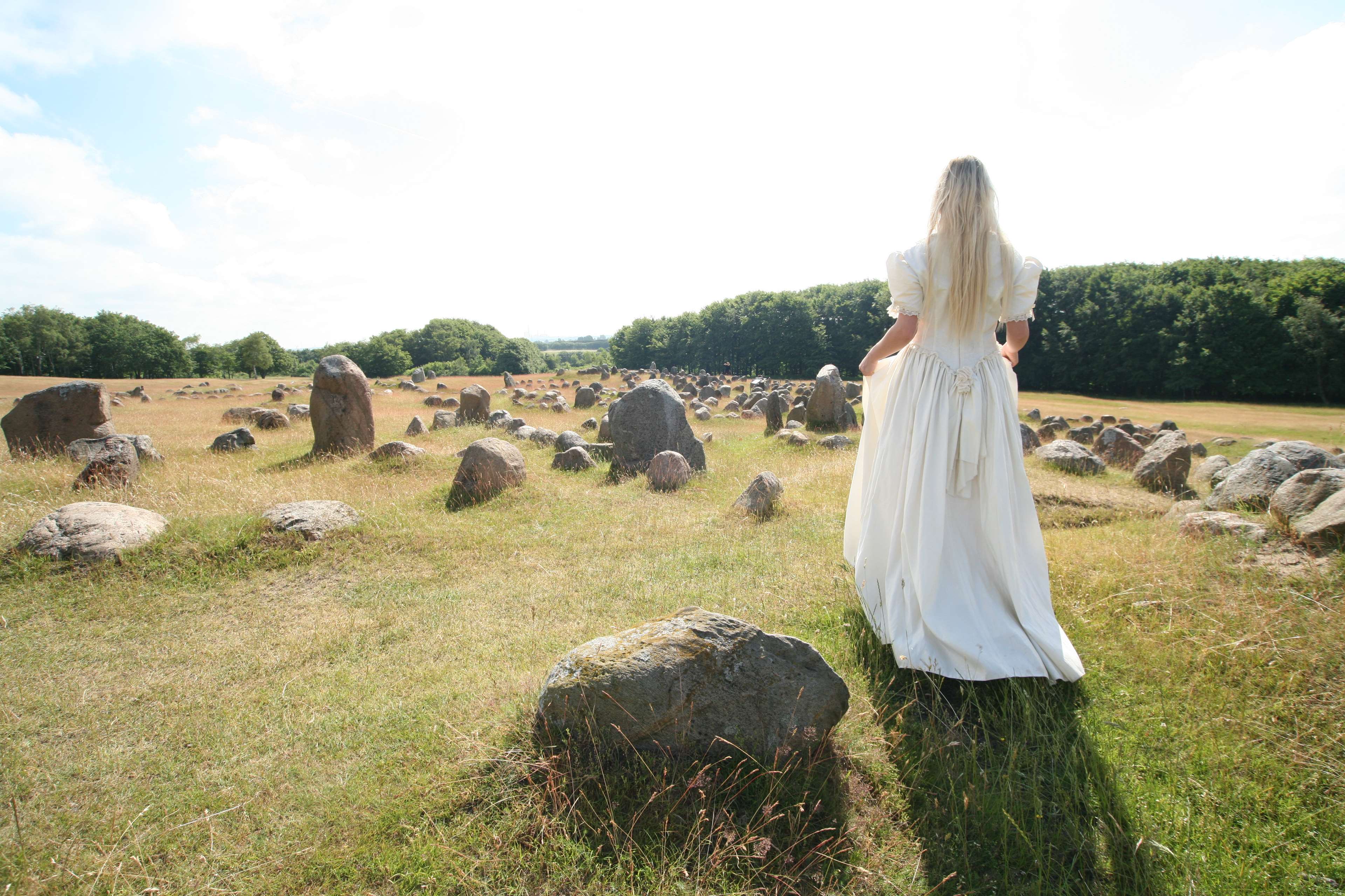 Woman in white dress walking through stone field HD Wallpaper