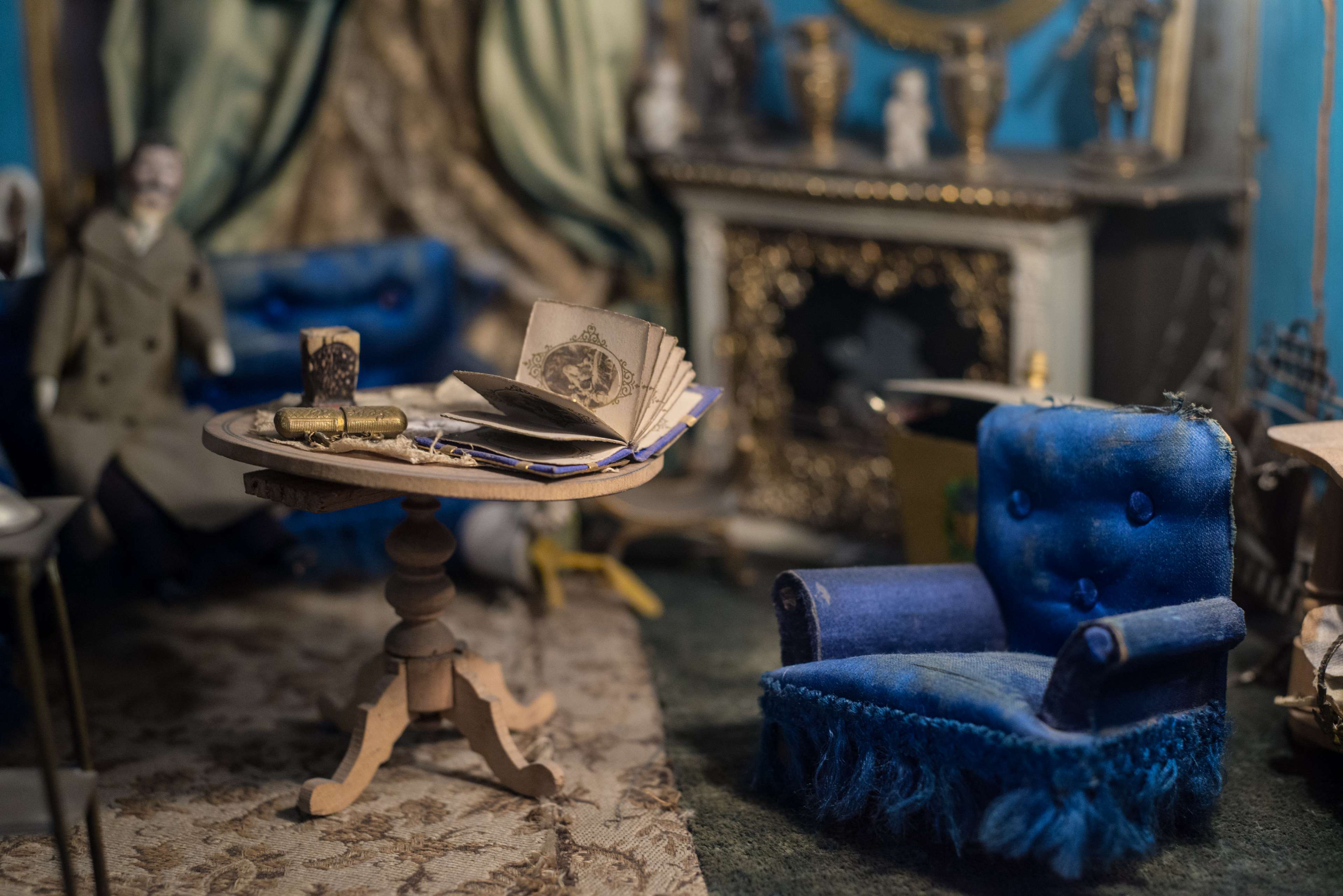 Miniature living room with doll, table, and chair HD Wallpaper