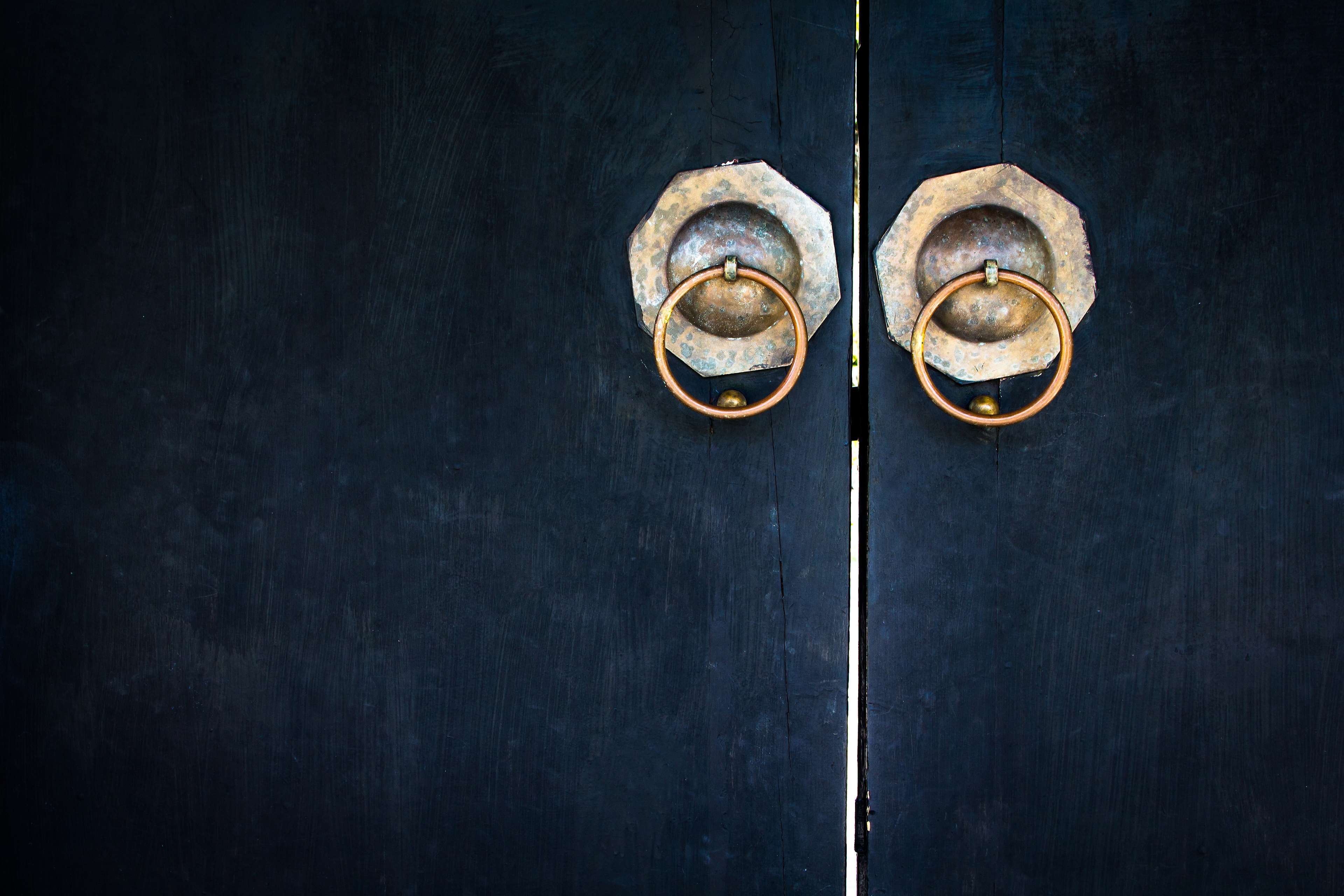 Antique brass door knockers on a dark wooden door HD Wallpaper