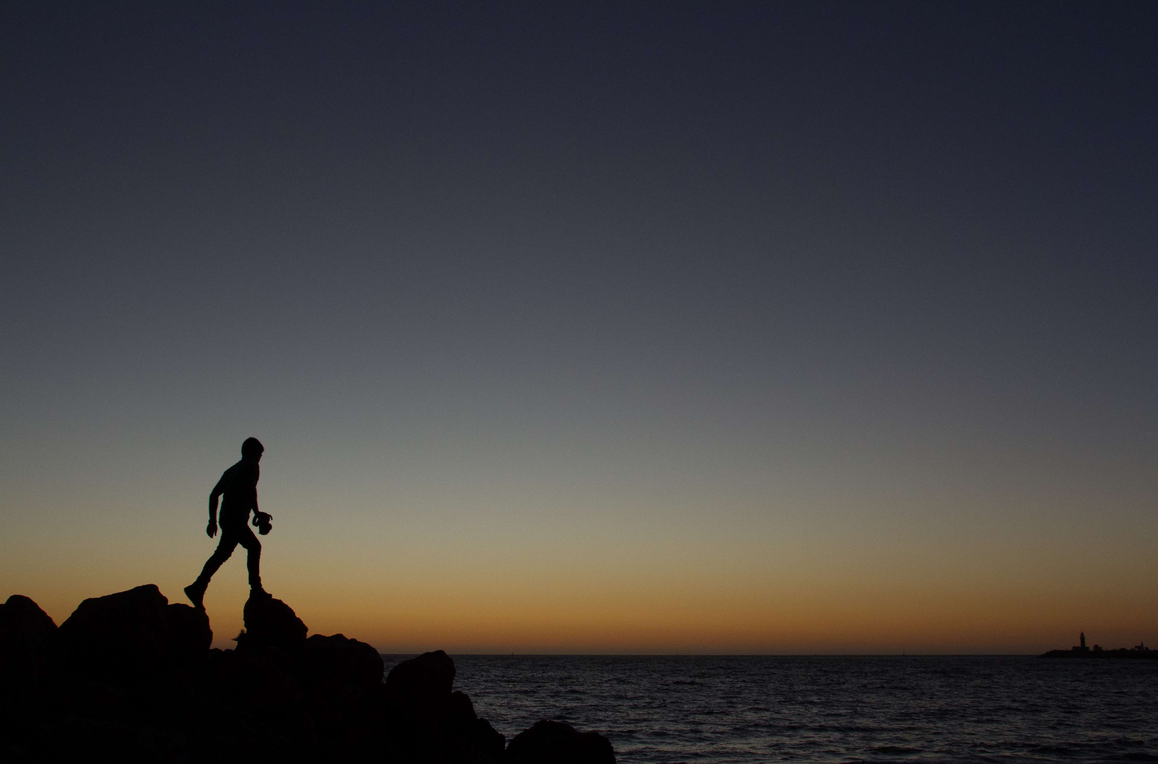 Silhouette of a person walking on rocks at sunset HD Wallpaper