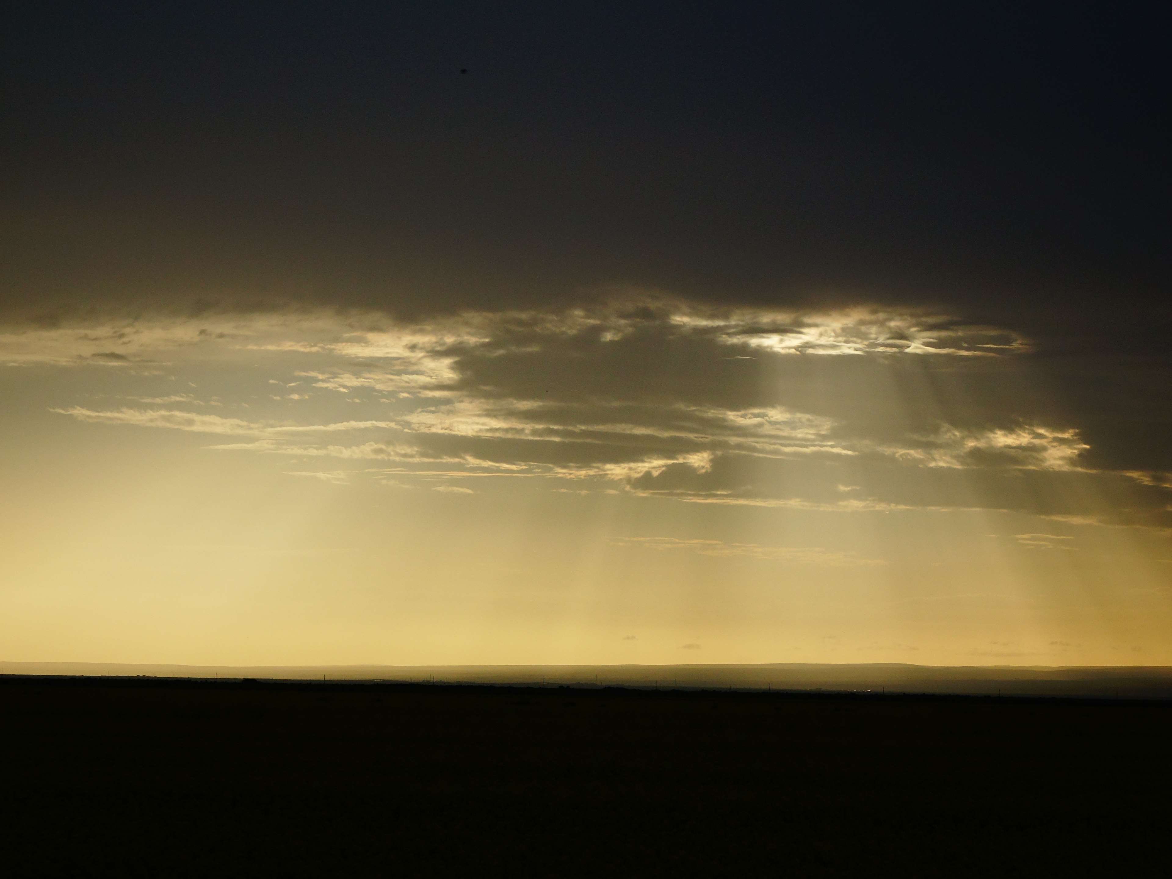 Sunbeams through clouds over a dark landscape HD Wallpaper