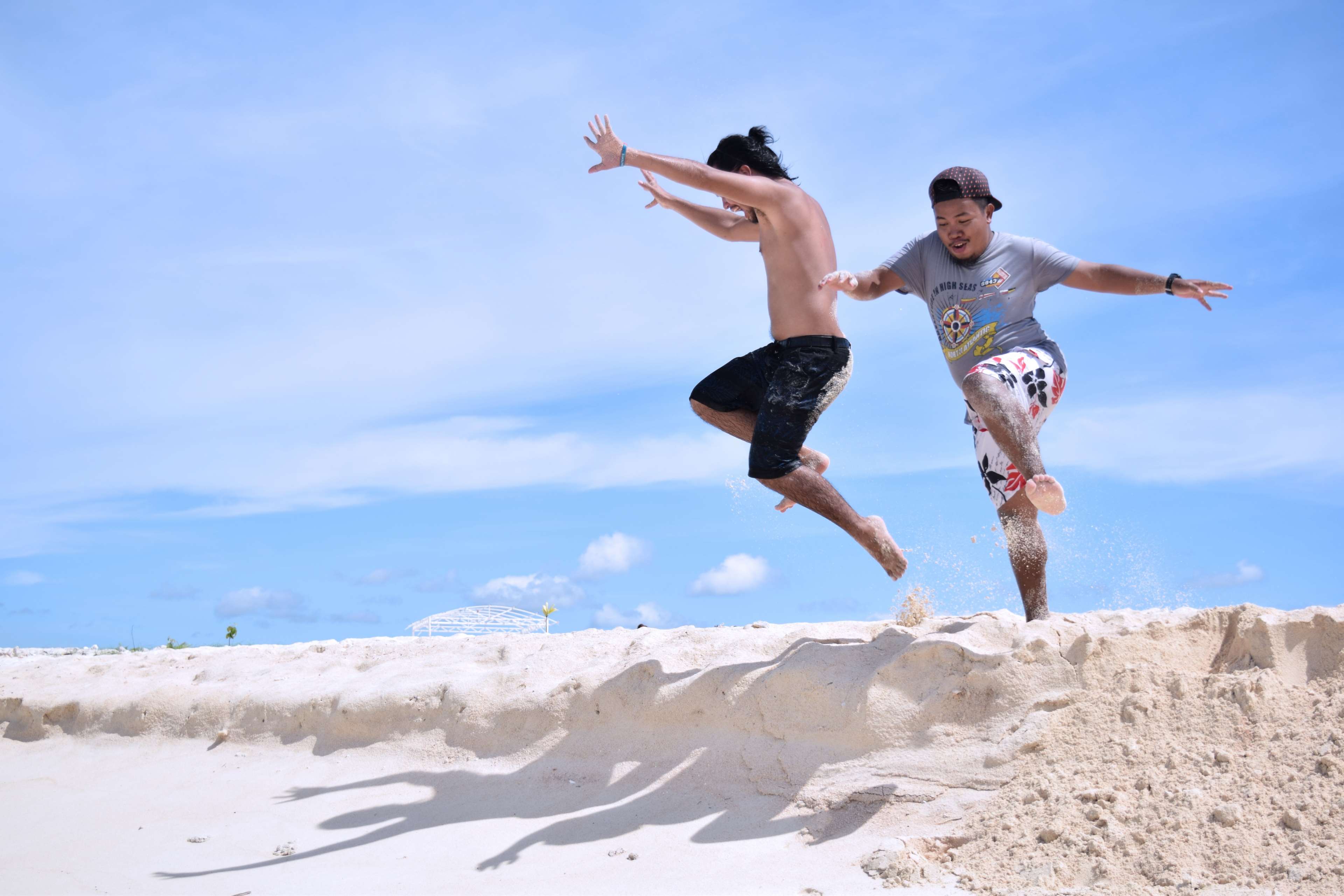 Two boys jumping on a sandy beach HD Wallpaper