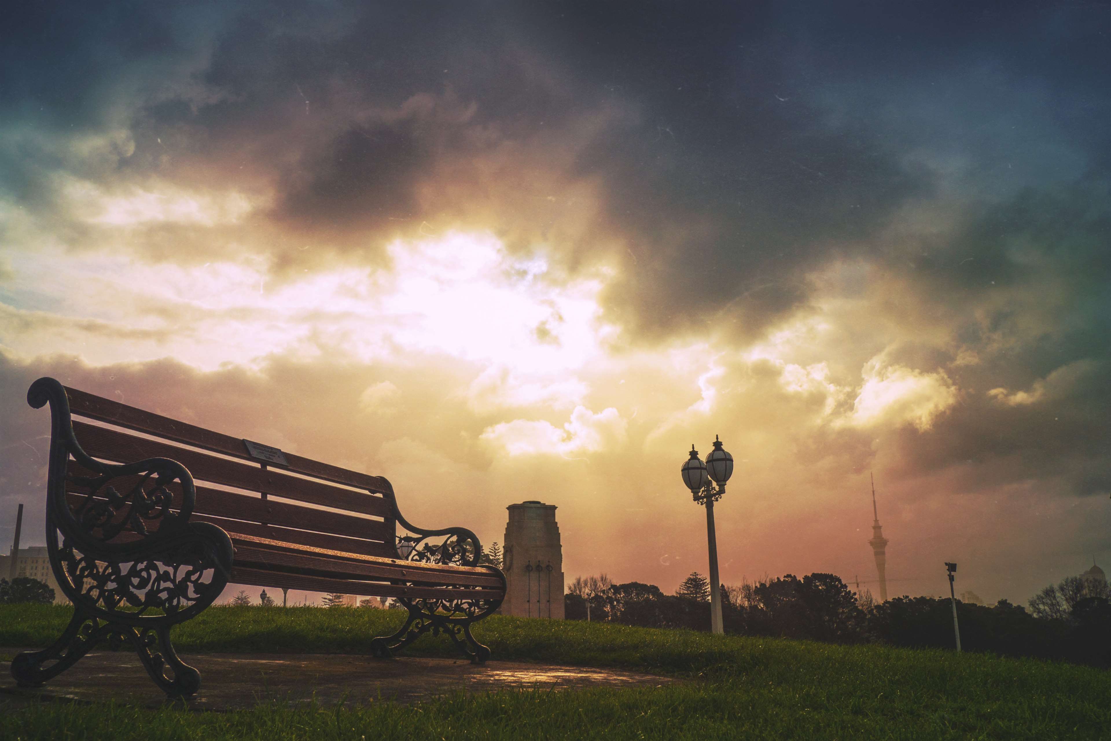 Park bench at dusk with cloudy sky and tower HD Wallpaper