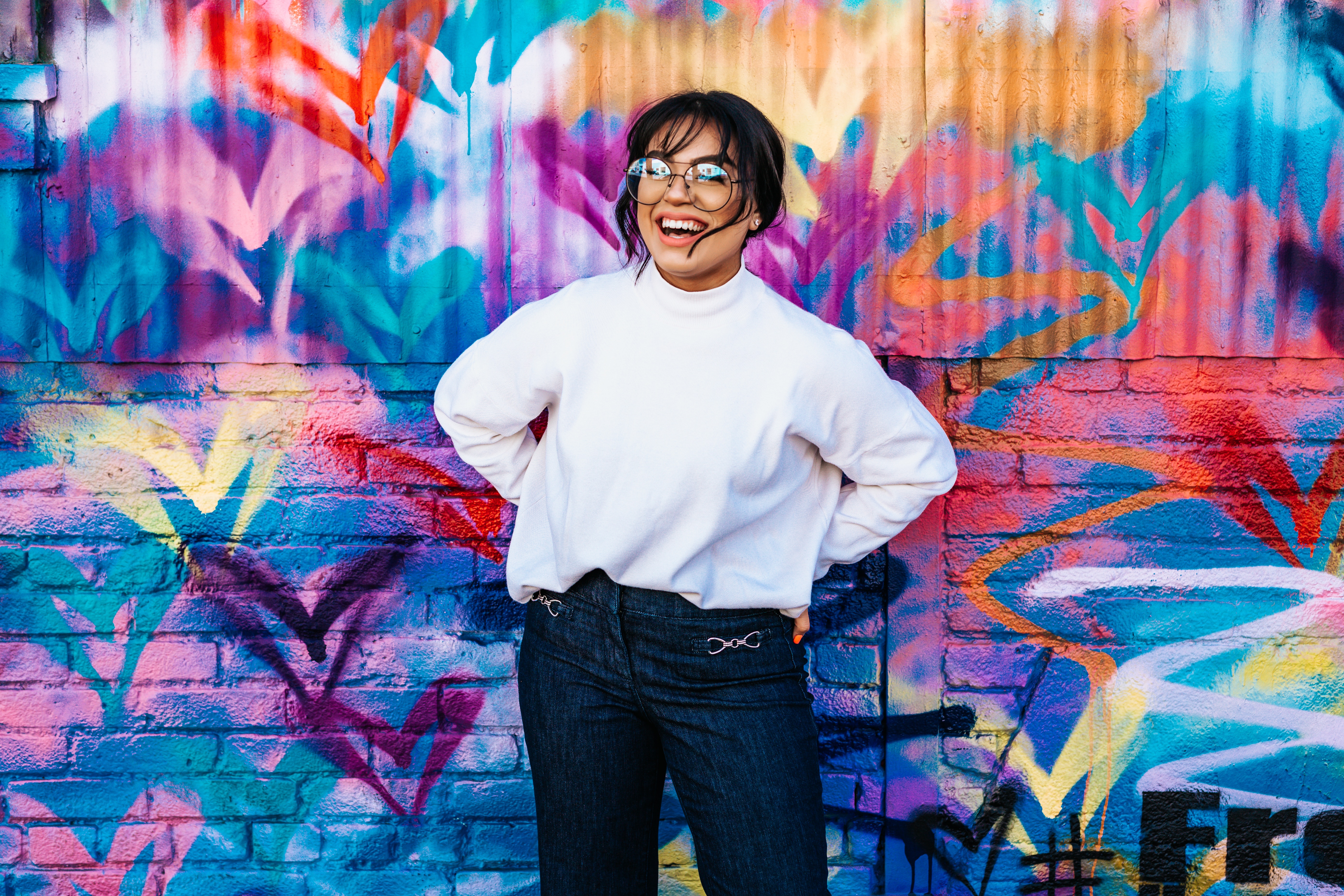 Woman in white sweater and jeans posing against graffiti wall HD Wallpaper