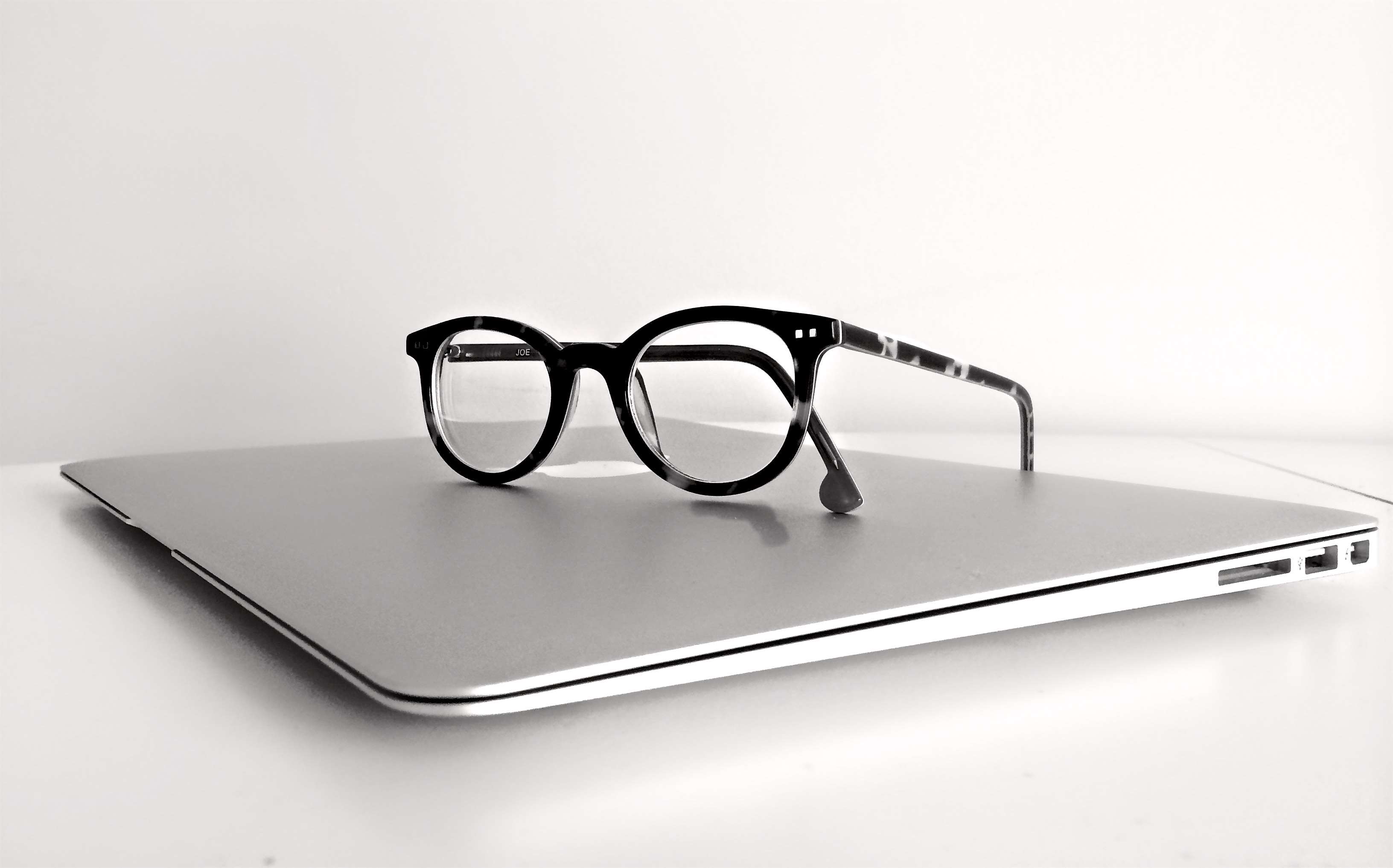 Black eyeglasses on a silver laptop HD Wallpaper