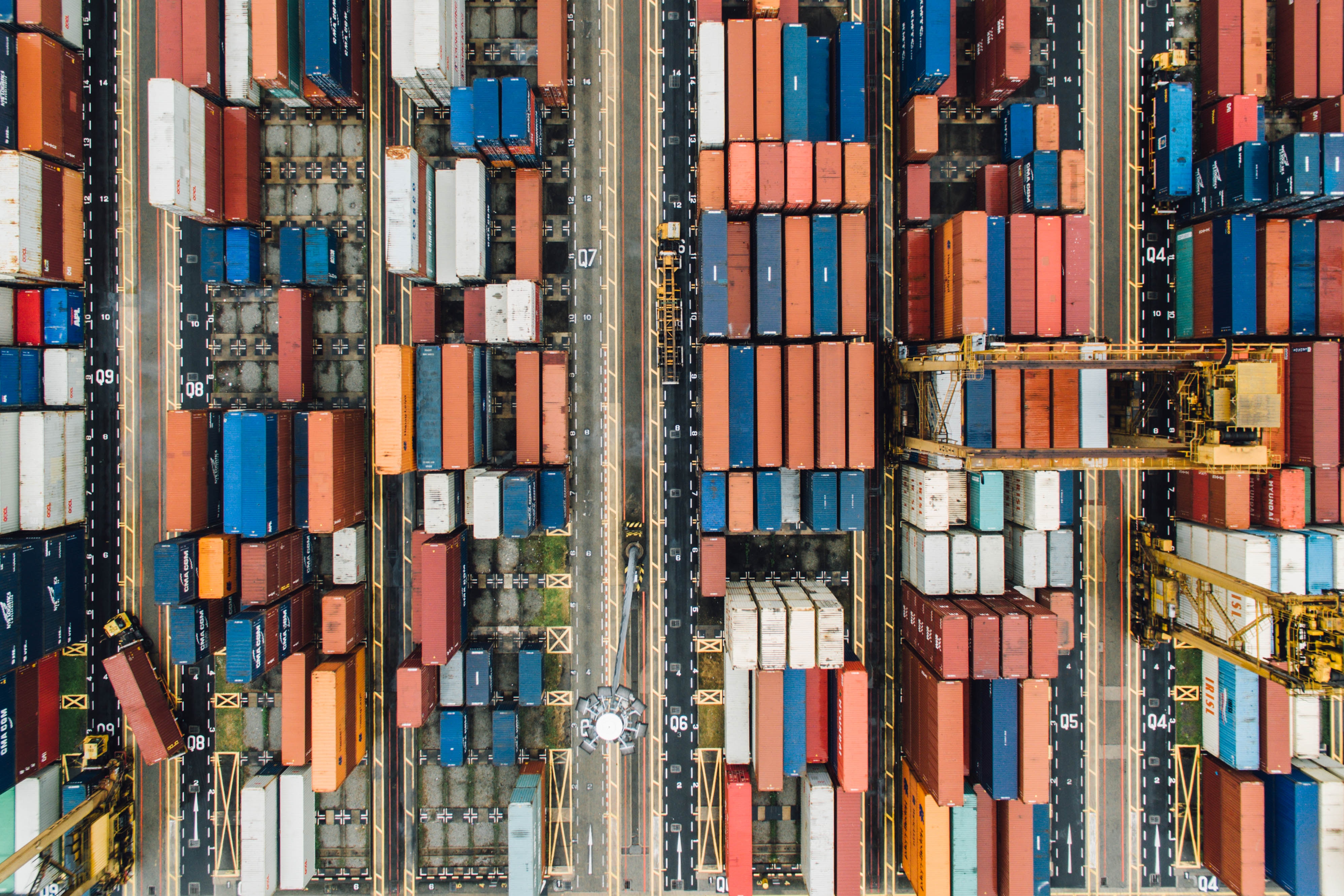 Aerial view of a container port with gantry cranes and stacks of shipping containers. HD Wallpaper