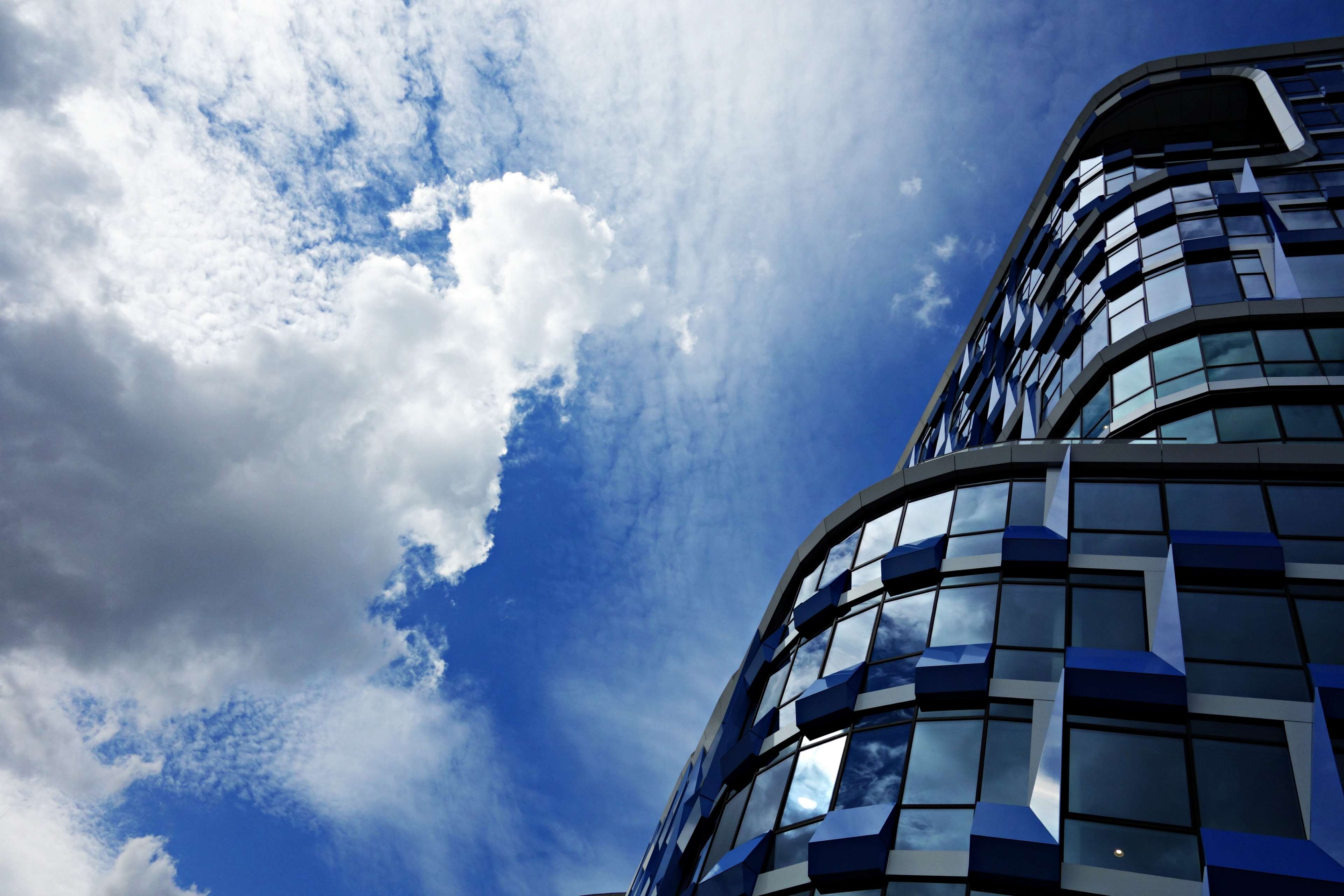 Modern blue glass building against a cloudy sky HD Wallpaper