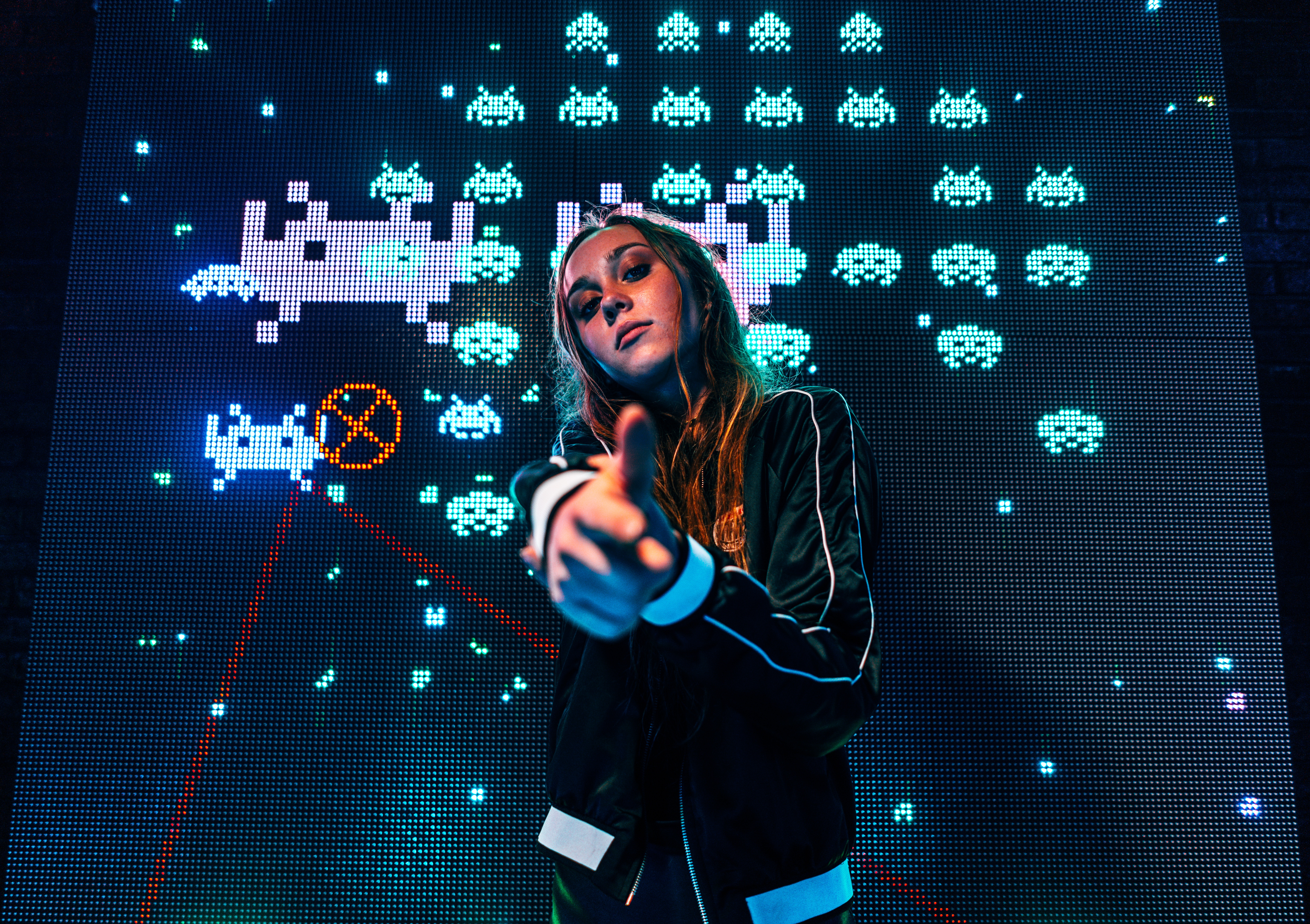 Young girl with finger gun in front of arcade screen HD Wallpaper