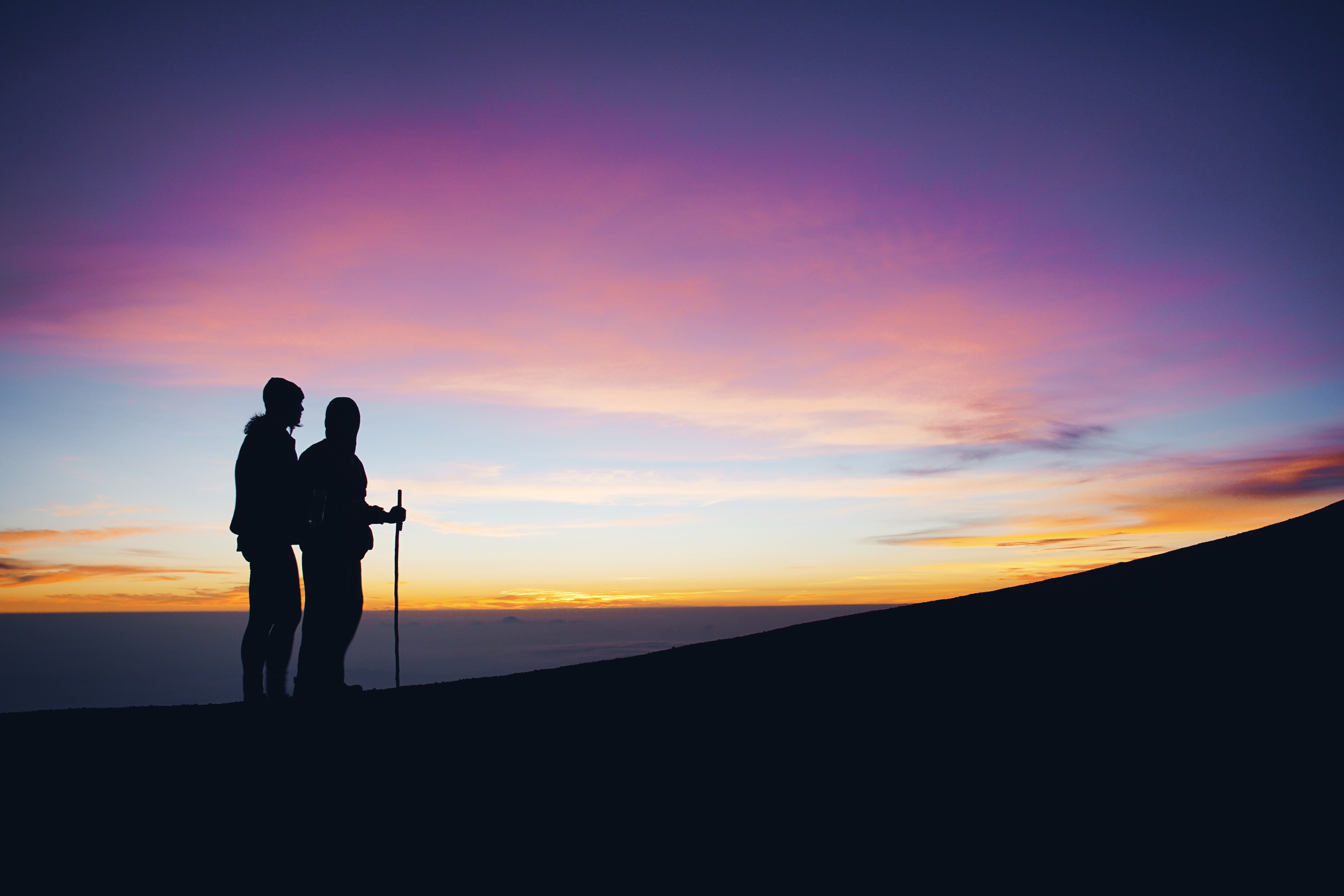 Two hikers silhouetted against a colorful sunrise sky HD Wallpaper