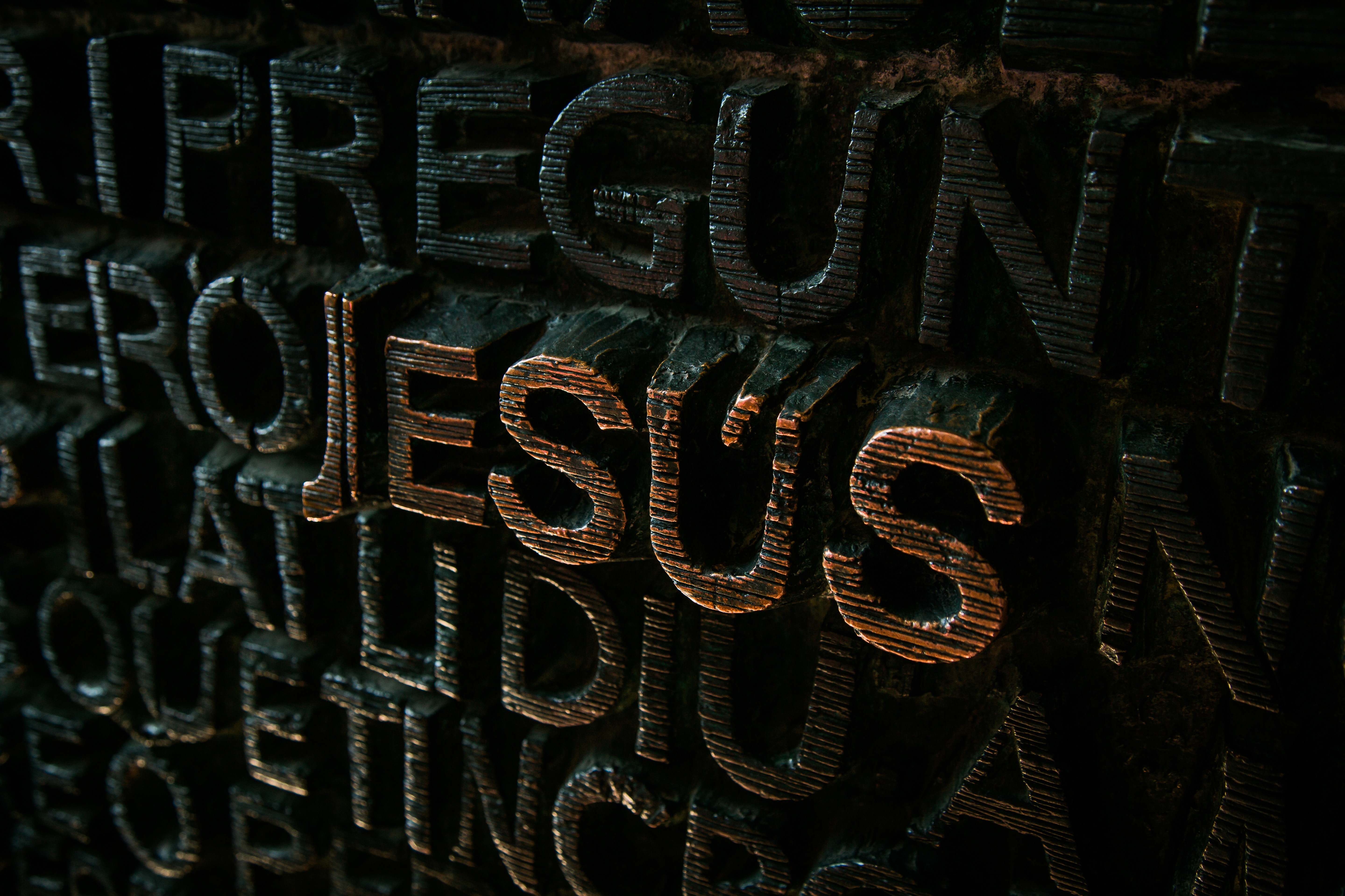 Close-up of carved letters spelling "JESUS" on a dark surface HD Wallpaper